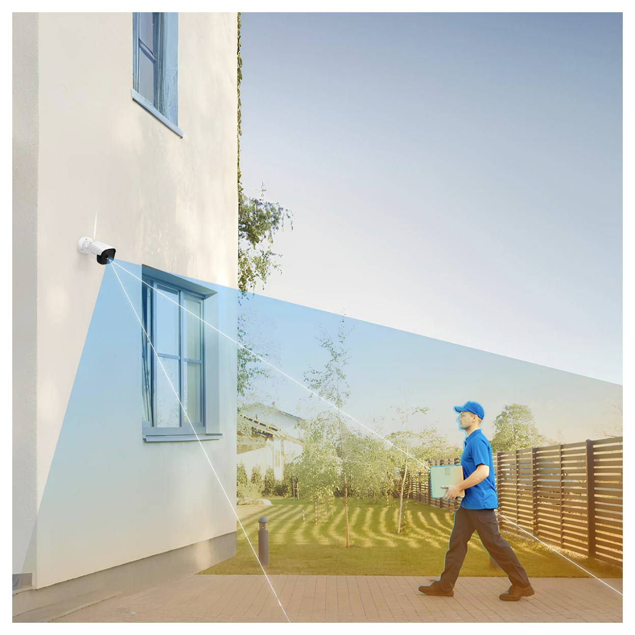 Eine Sicherheitskamera an einer Gebäudewand überwacht einen Mann in blauer Uniform, der ein Paket in einem Hof mit Bäumen und einem Zaun trägt.