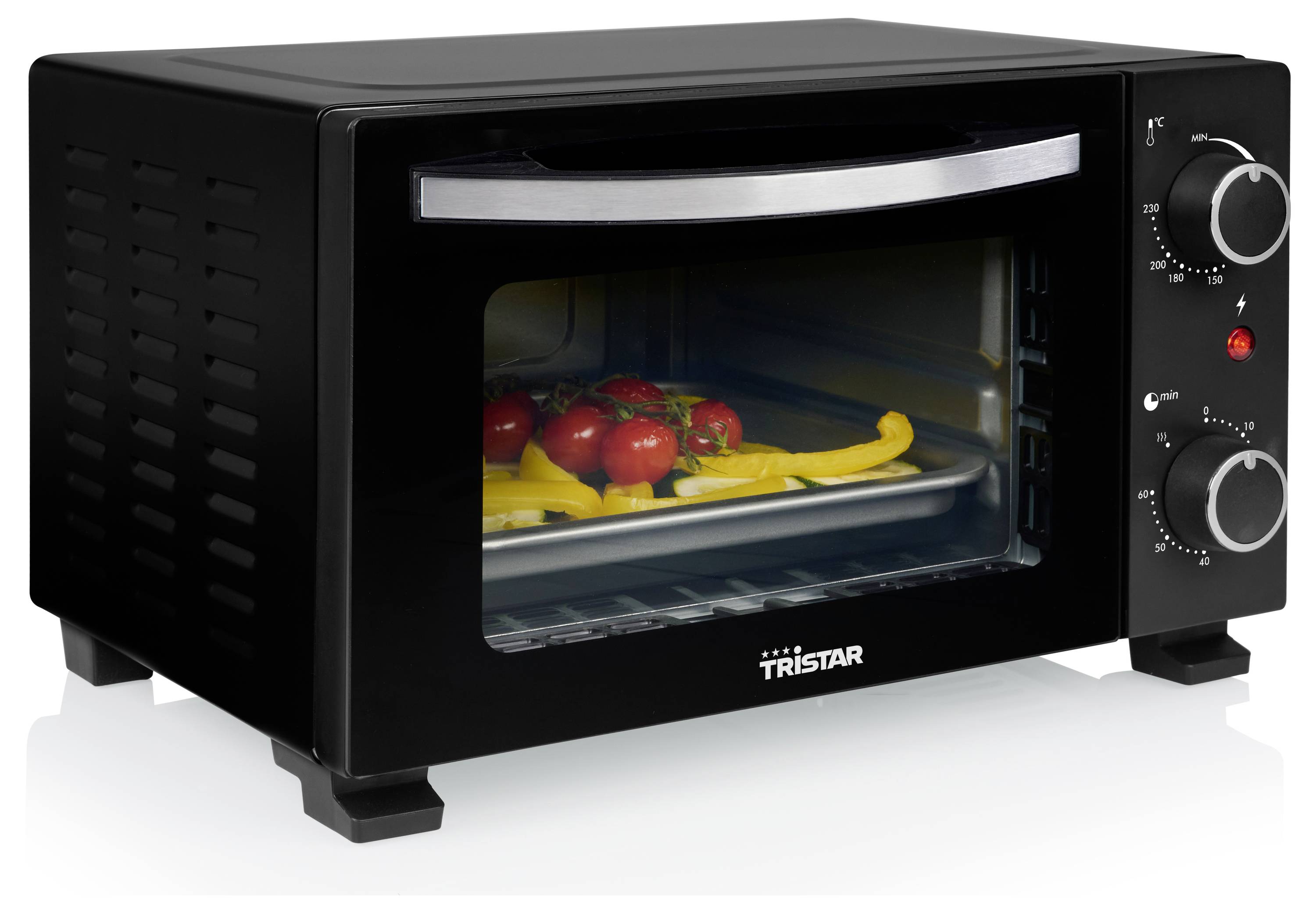 Ein kleiner schwarzer Ofen mit Chromgriff und Bedienknöpfen. Im Inneren liegt auf einem Backblech eine Auswahl an gehackten roten und gelben Paprikaschoten sowie Tomaten.