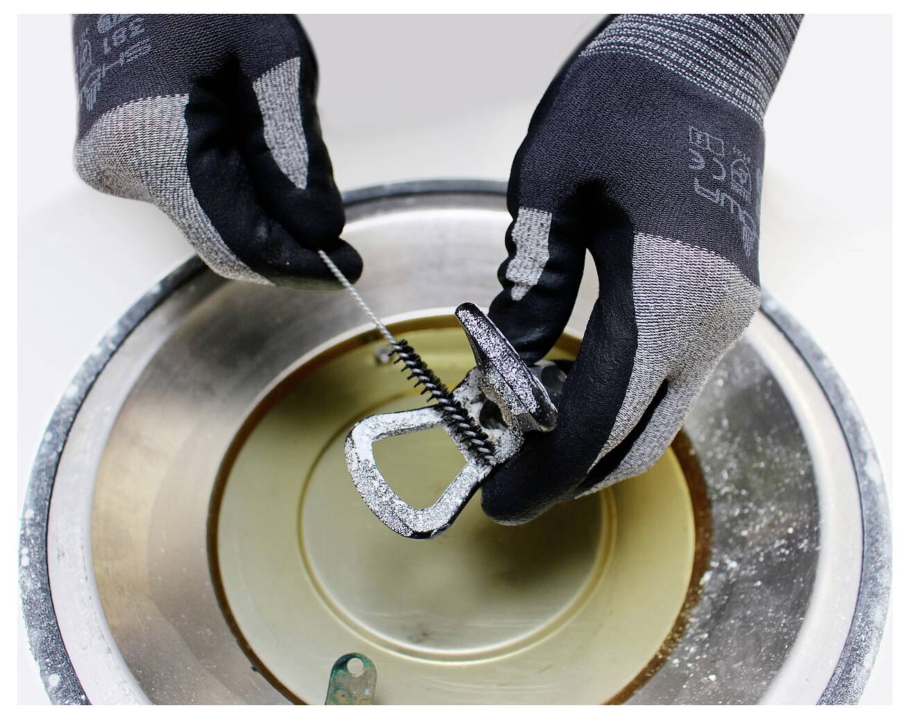 Behandschuhte Hände verwenden einen Rohrabschneider, um ein Metallrohr über einer Schale zu durchtrennen und zeigen damit einen Arbeitsschritt in der Klempnerei oder beim Metallschneiden.