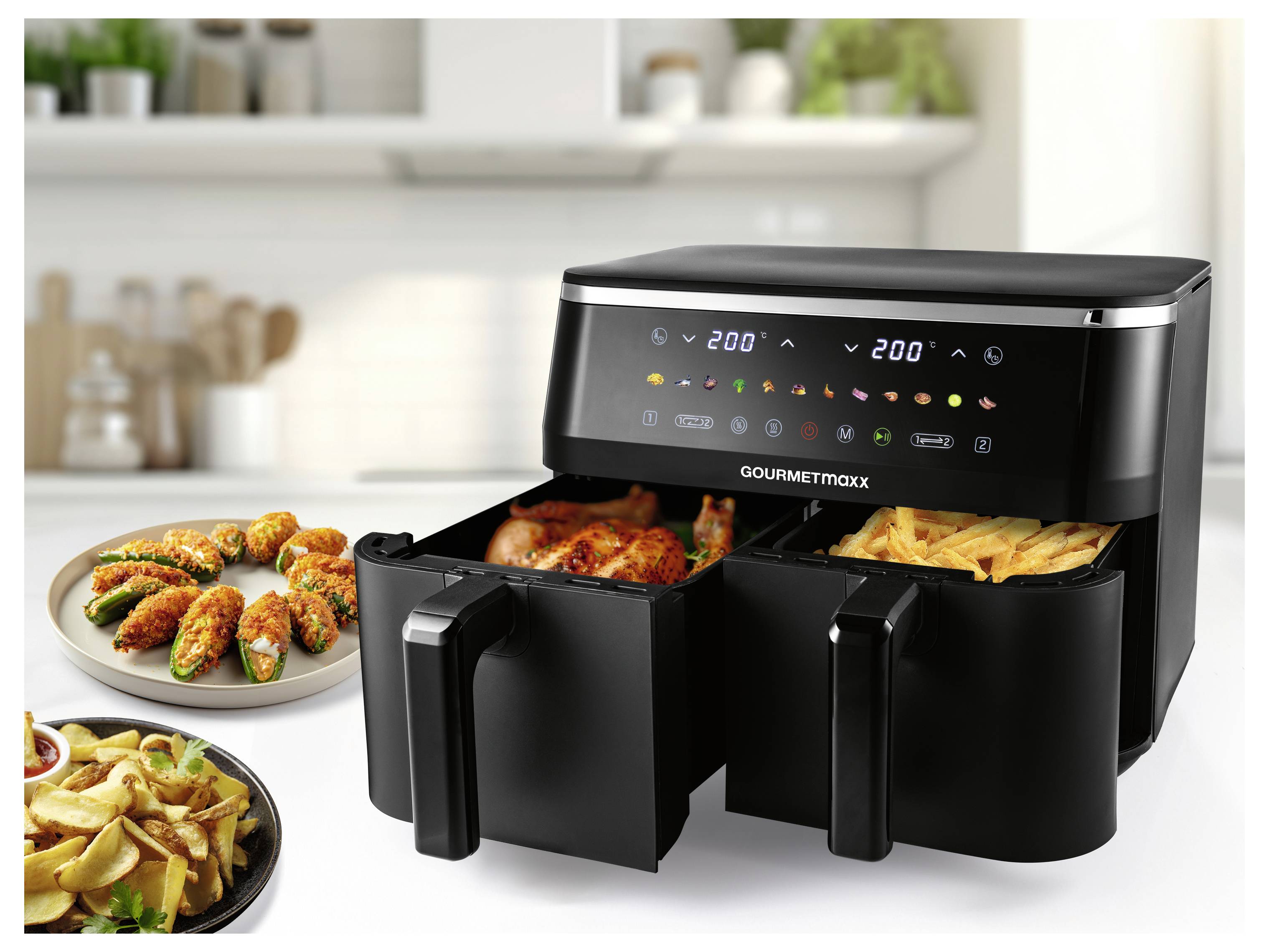 Ein Doppelkorb-Heißluftfritteur steht auf einer Küchenarbeitsplatte und zeigt ein digitales Display mit Kocheinstellungen. In der Nähe befinden sich auf Tellern gebratenes Hähnchen, Pommes und gefüllte Paprikaschoten.