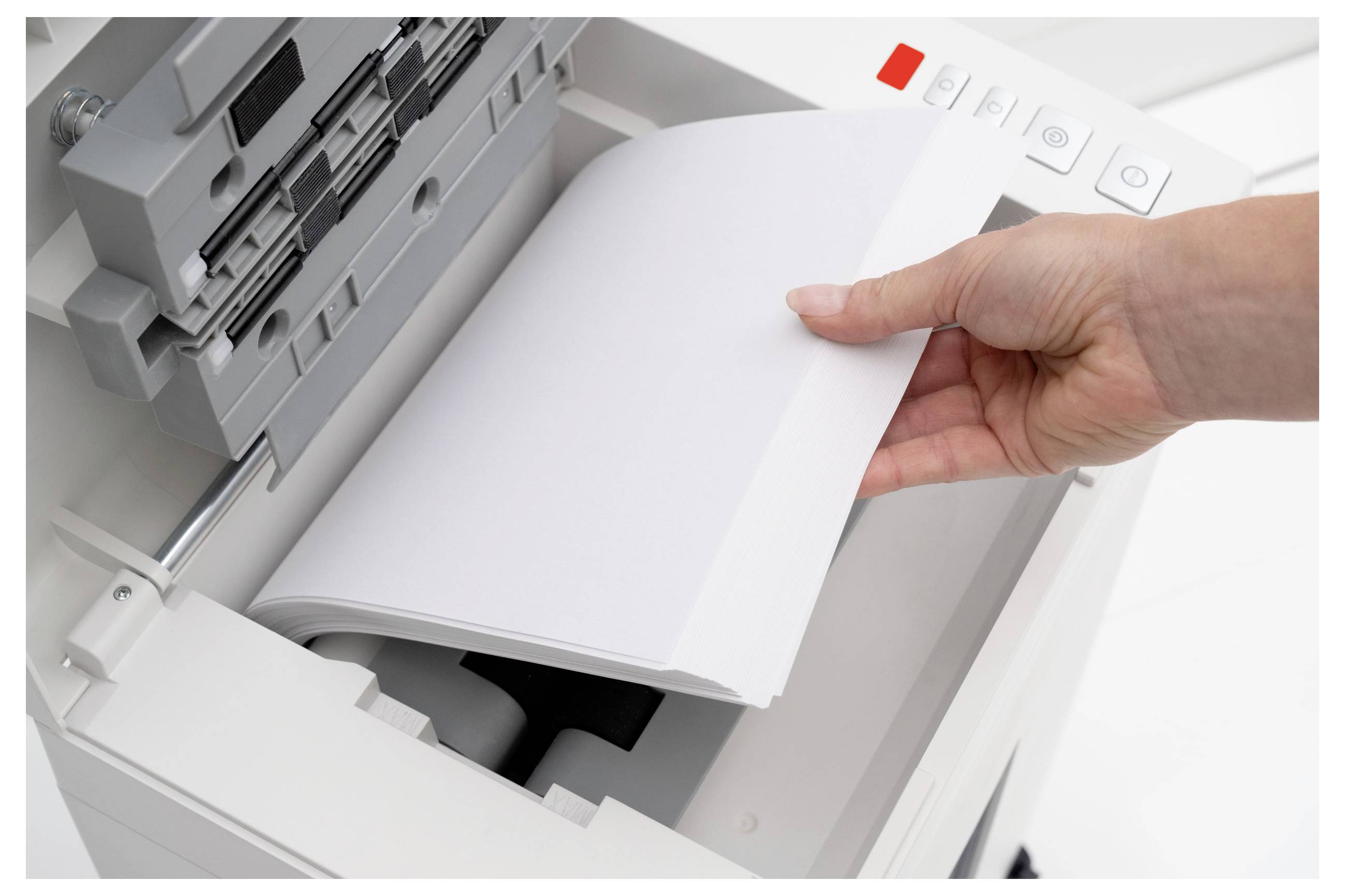 Eine Hand legt Papier in den Papierschacht eines Kopierers und bereitet sich auf das Drucken vor. Der Kopierer verfügt über sichtbare Bedienknöpfe an der Seite.