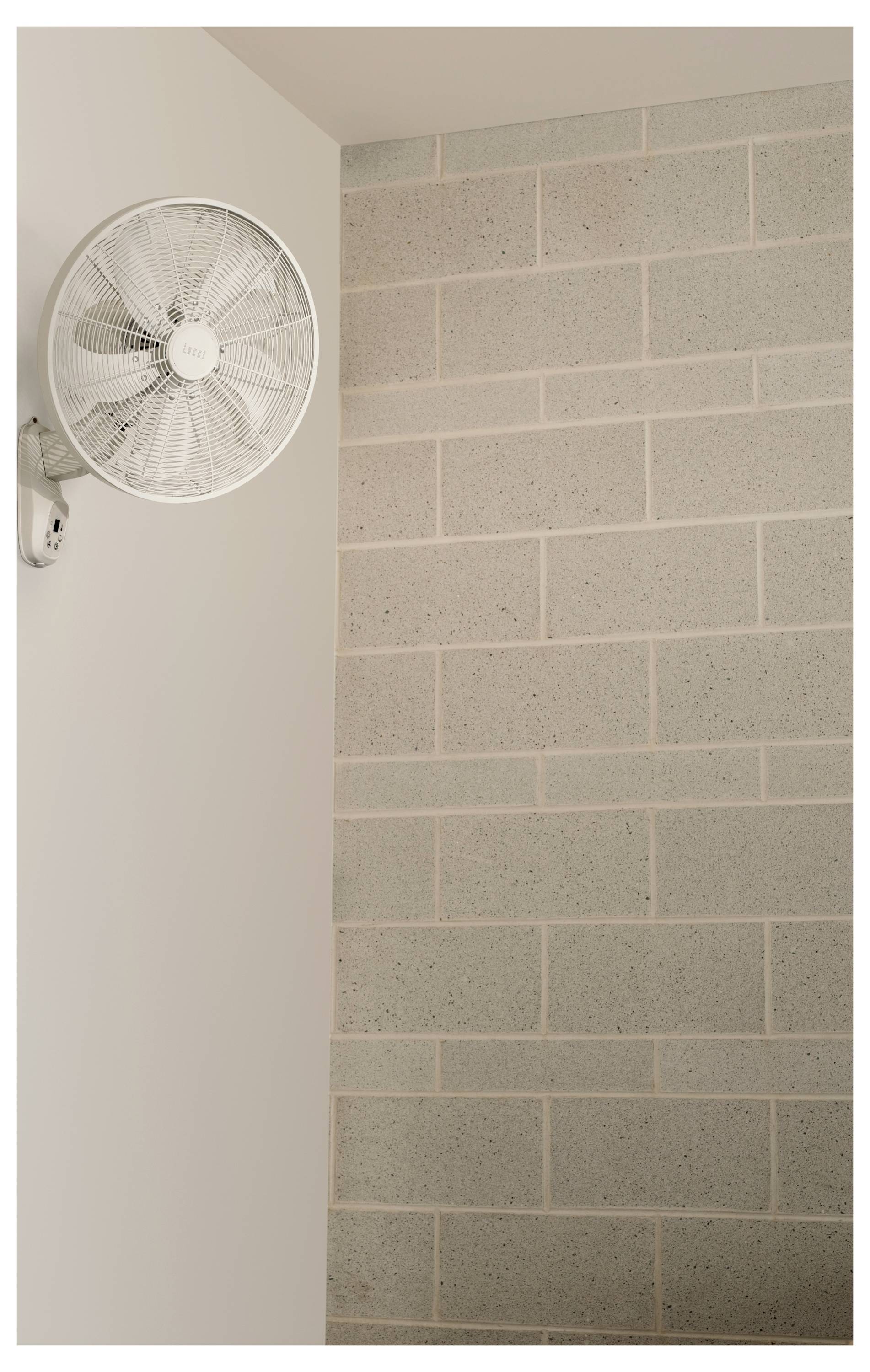 Eine weiße Wandventilator an der Wand auf der linken Seite, daneben eine Wand aus grauen Ziegelsteinen.