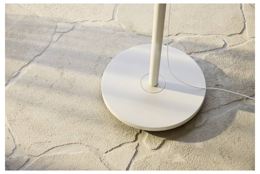 Eine weiße, runde Lampenfassung mit angeschlossenem Kabel sitzt auf einem strukturierten Steinboden, während das Sonnenlicht weiche Schatten über die Oberfläche wirft.