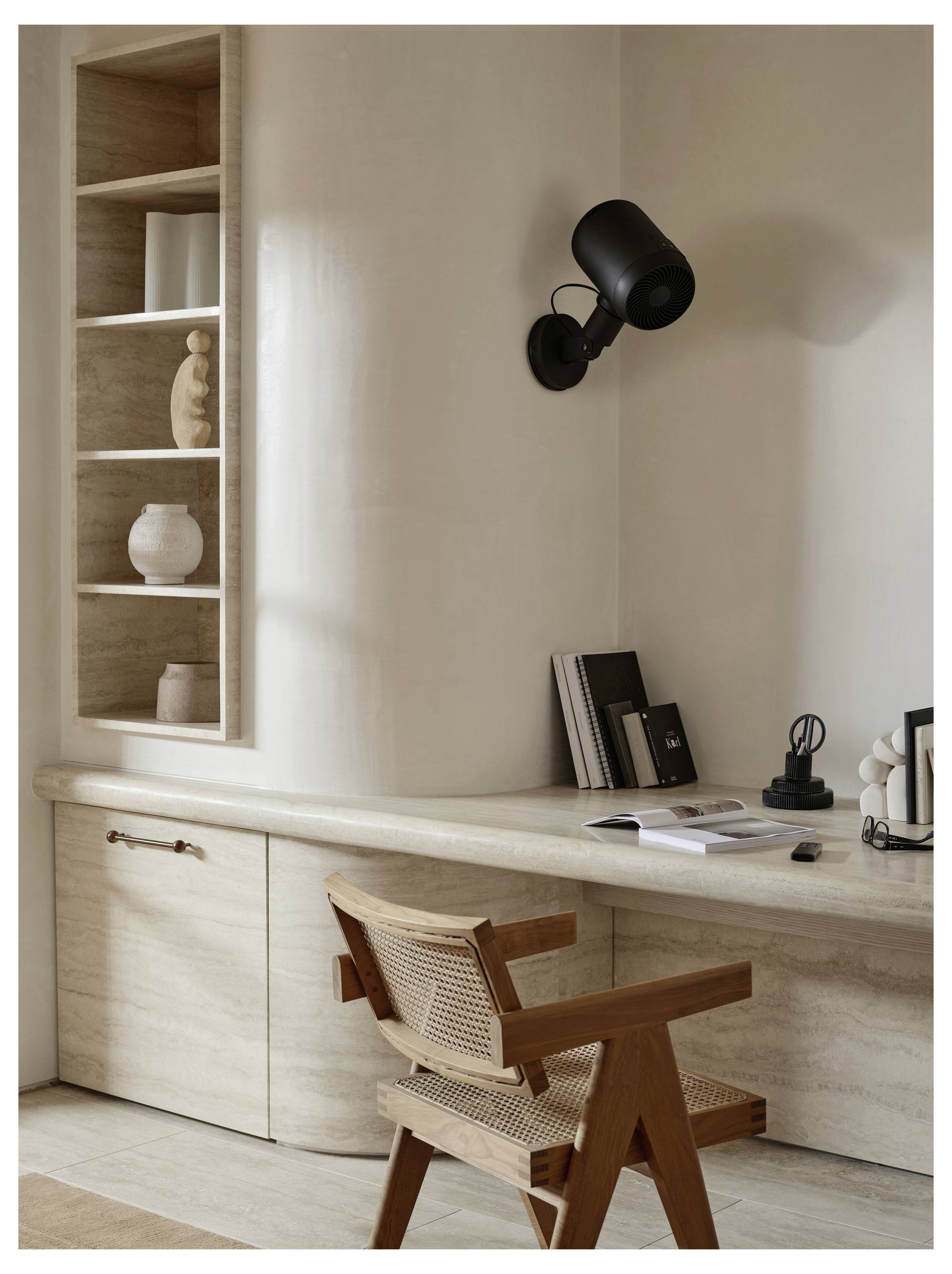 Eine minimalistische Hausarbeitsecke mit einem Holzschreibtisch und -stuhl, einer wandmontierten schwarzen Lampe und Regalen, die Dekoartikel und Bücher tragen.