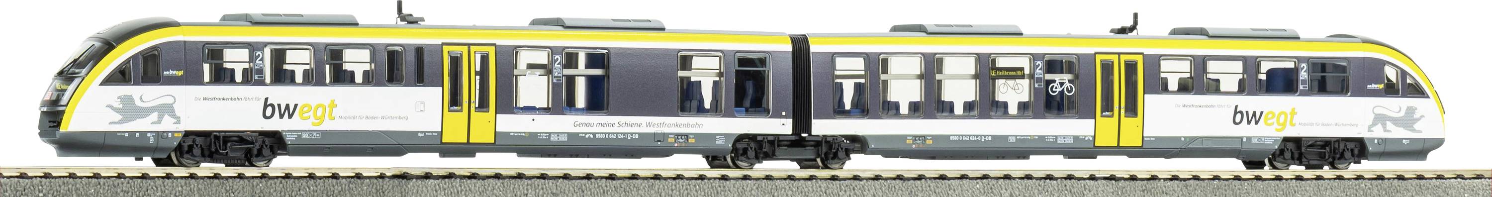 Ein Modelleisenbahn auf Gleisen mit einem hellgrauen und gelben Design, das das Logo „bwegt