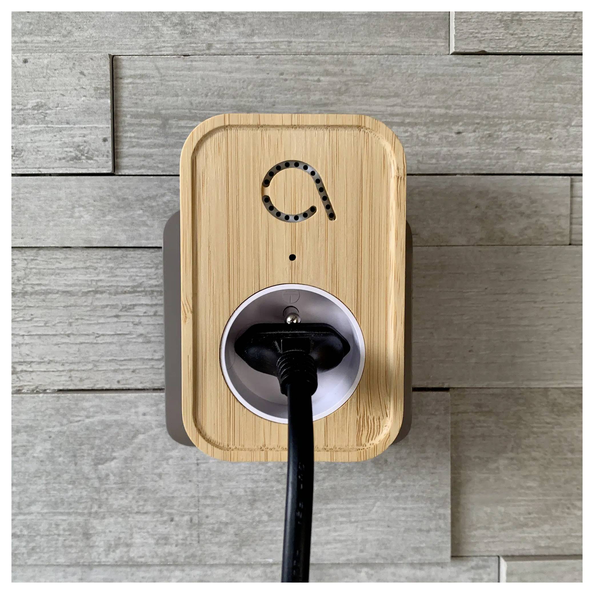 Ein Smart-Stecker im Holz-Design, der an einer grauen gefliesten Wand montiert ist, mit einem schwarzen Kabel, das in seine Buchse gesteckt ist und ein Stromicon zeigt.