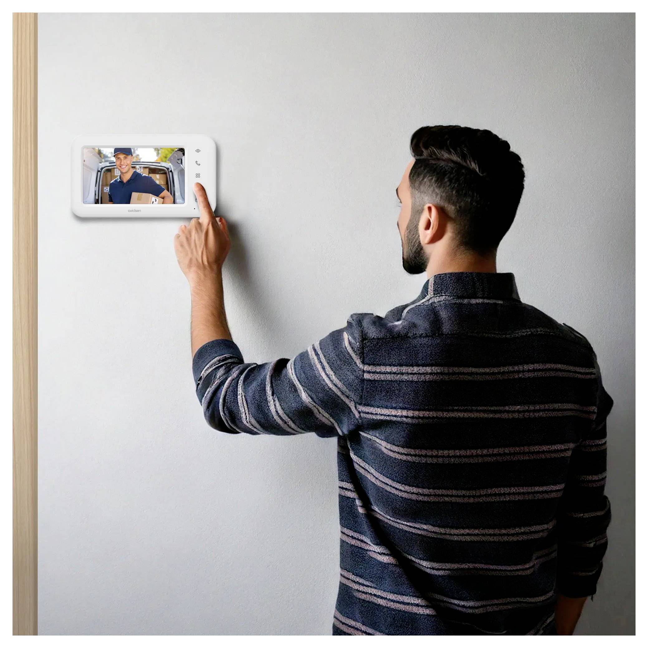 Ein Mann interagiert mit einem wandmontierten Touchscreen, der einen Videoanruf mit einem anderen Mann zeigt und dabei ein Smart-Home-Kommunikationsgerät andeutet.