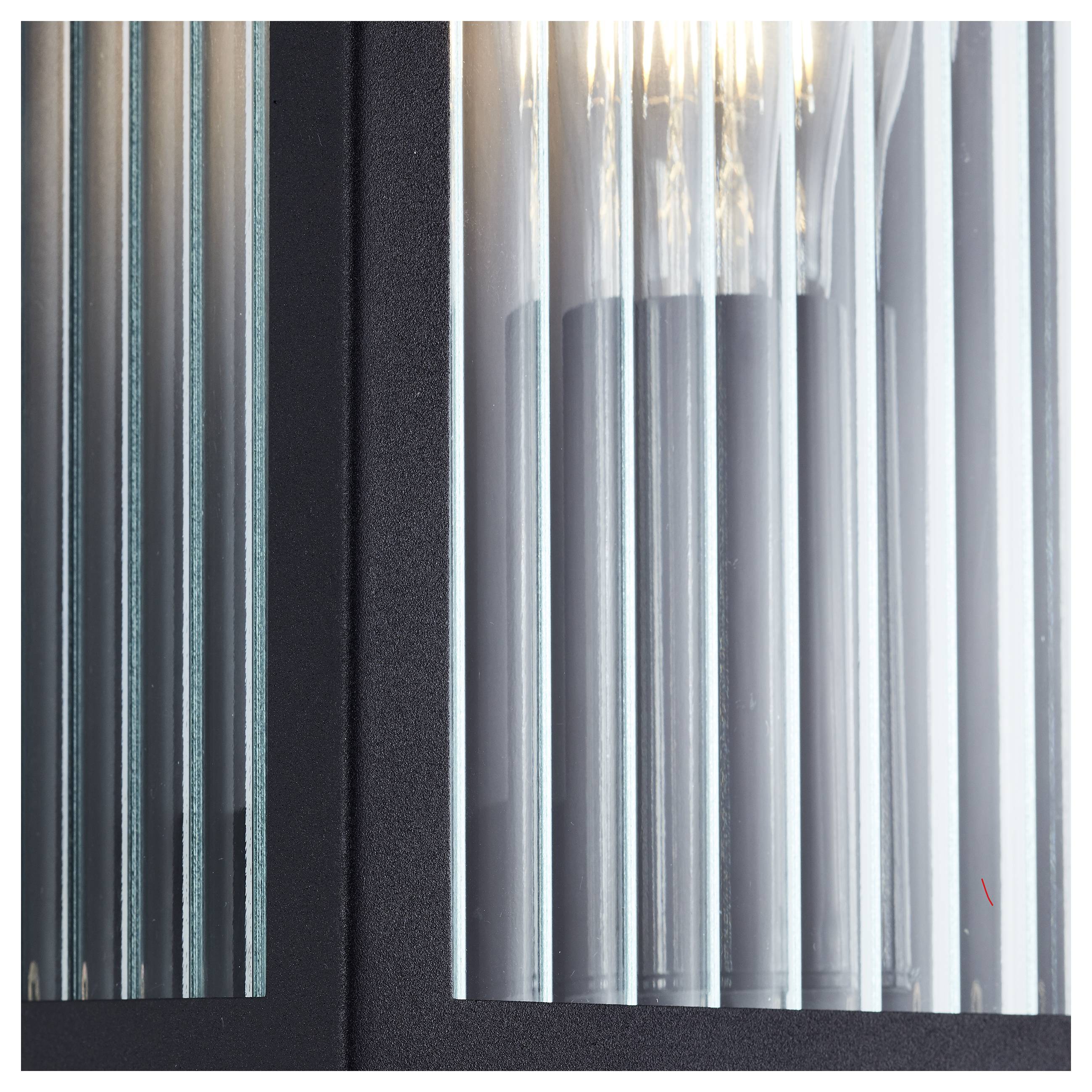 Eine Nahaufnahme einer modernen Glasleuchte mit vertikalen transluzenten Paneelen, vor einem schwarzen Hintergrund, die mehrere Glühbirnen zeigt.