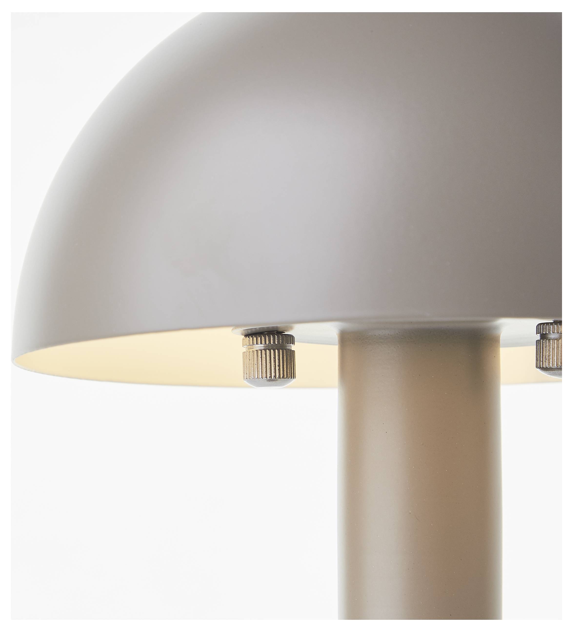 Eine Nahaufnahme einer modernen Lampe mit einem kuppelförmigen beigen Lampenschirm und Metallfassungen, die warm auf einem weißen Hintergrund beleuchtet ist.