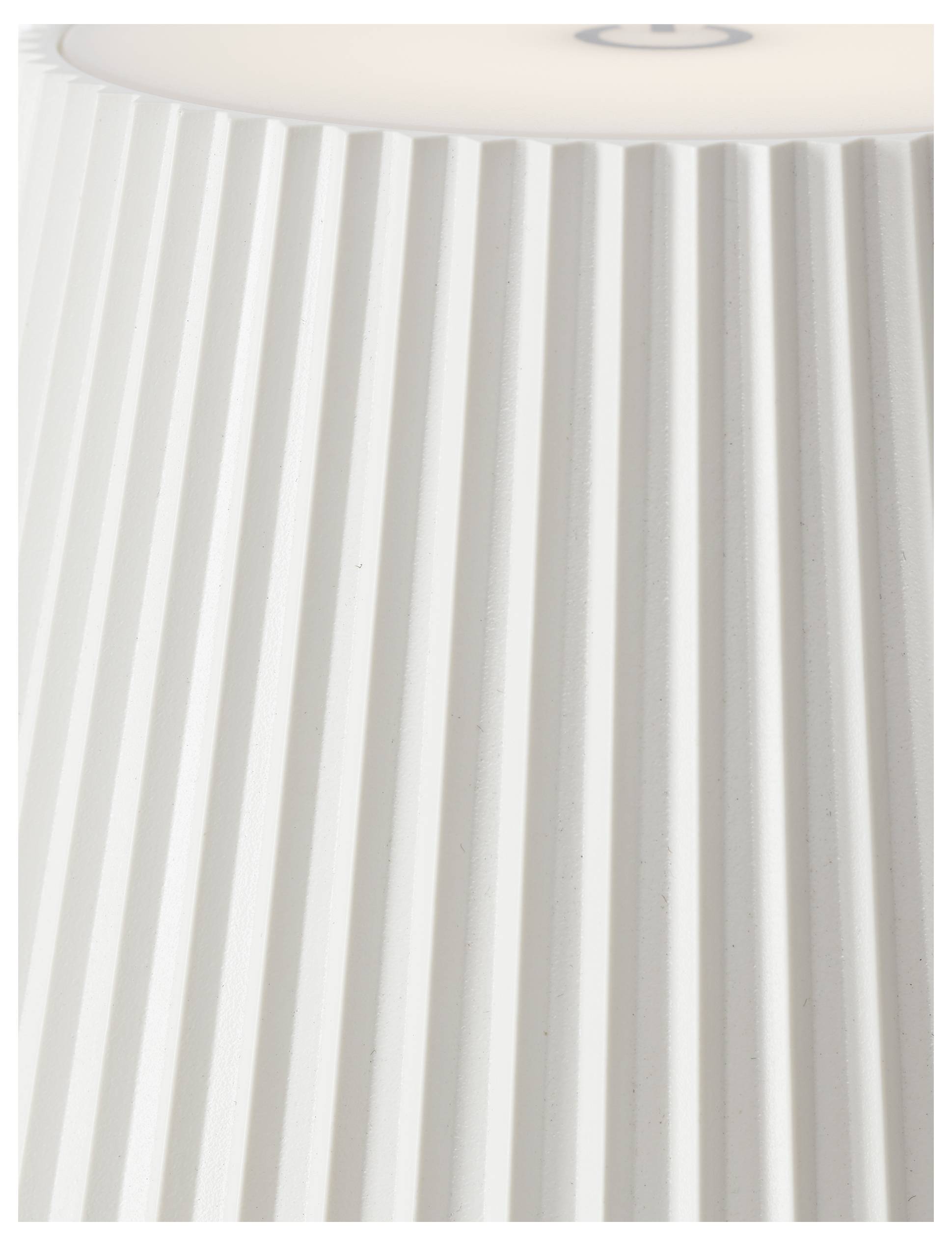 Eine Nahaufnahme eines weißen, gefalteten Lampenschirms mit vertikalen Rillen, der von oben teilweise beleuchtet wird.