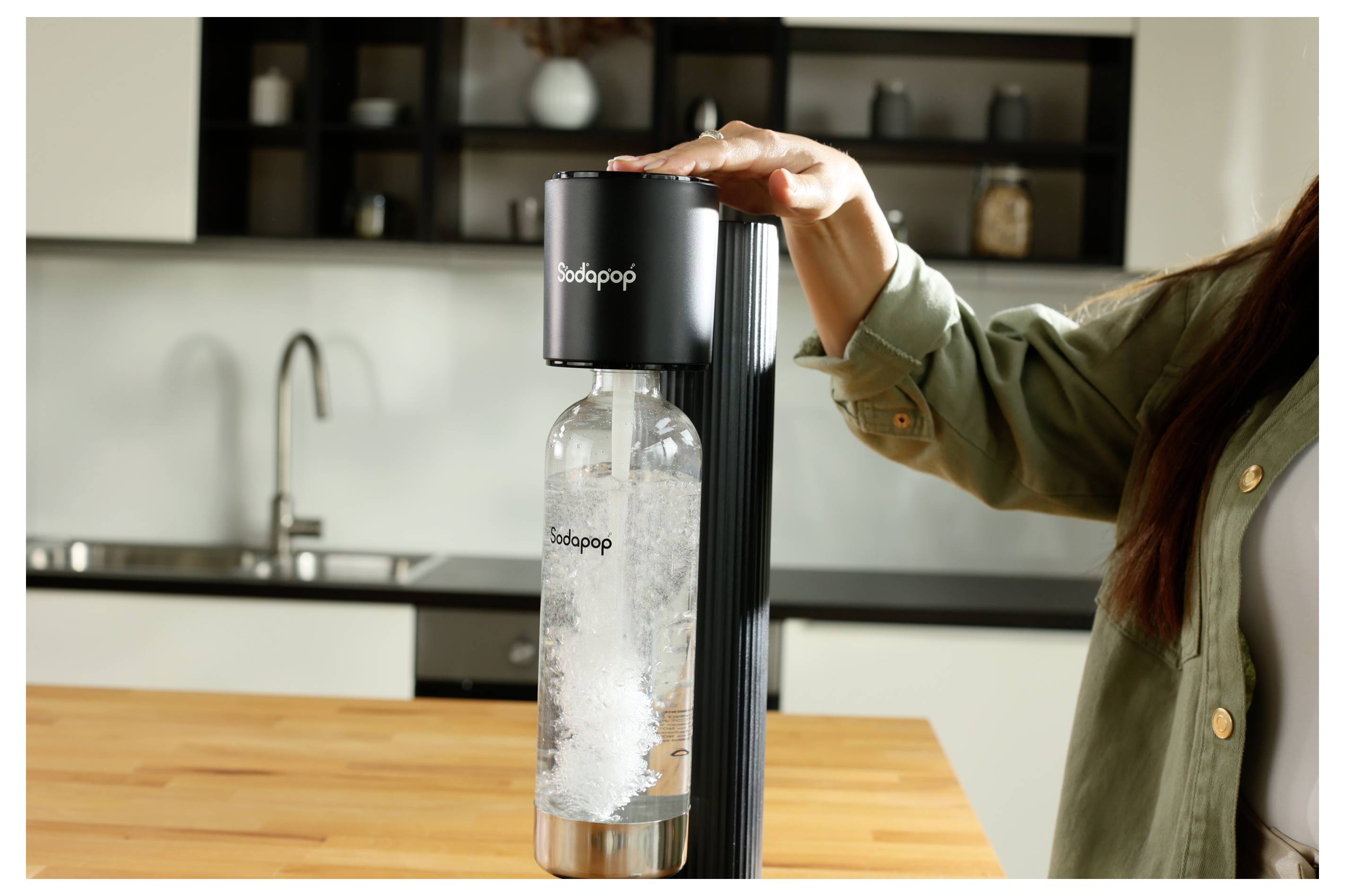 Eine Person, die in einer Küche einen schwarzen Sodabereiter verwendet, um Wasser zu karbonisieren.