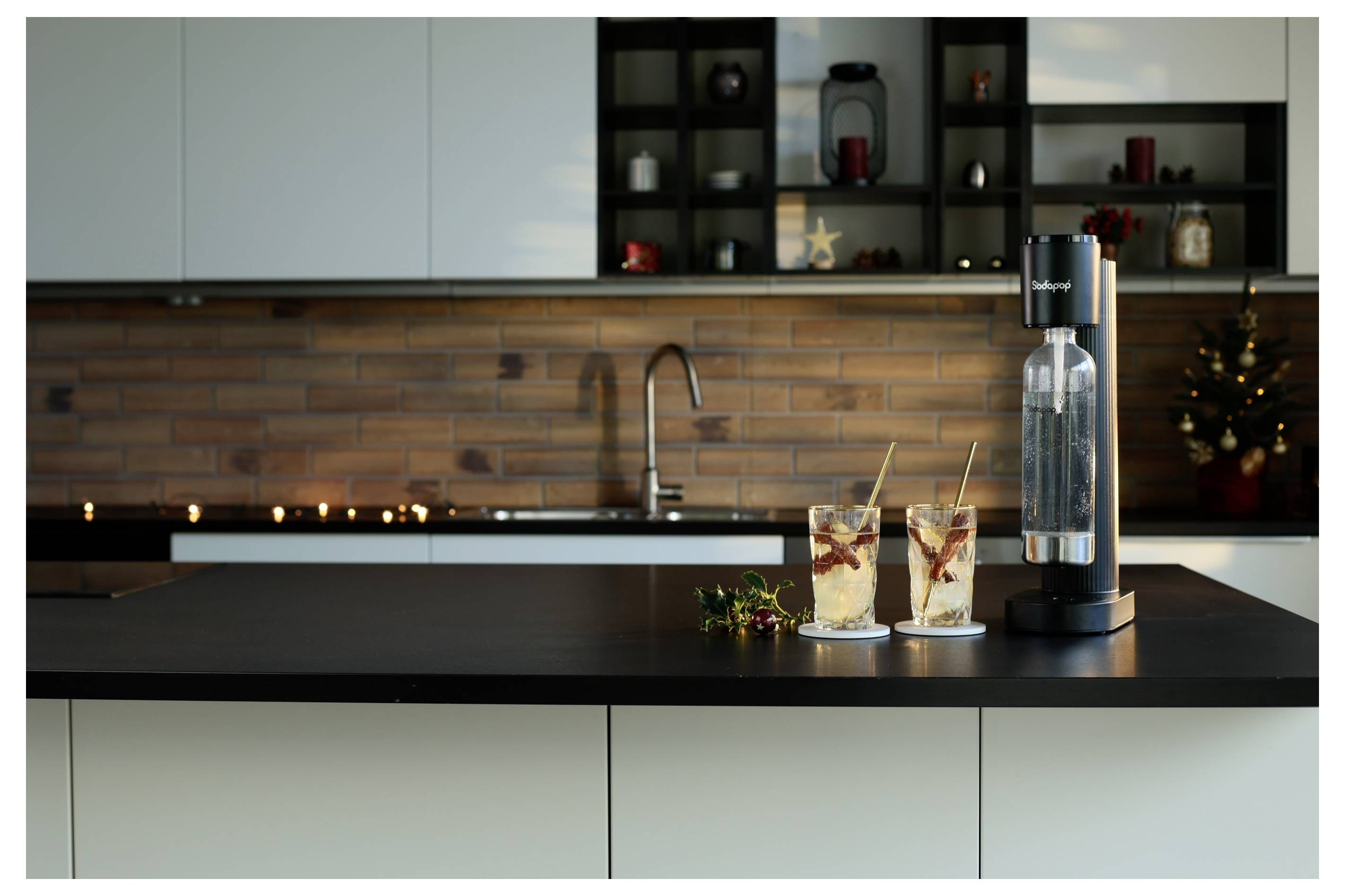 Moderne Küche mit schwarzer Arbeitsplatte, Wassersprudler und zwei Gläsern Eiskaffee mit Strohhalmen. Ziegelwand-Rückwand und sanfte Beleuchtung.