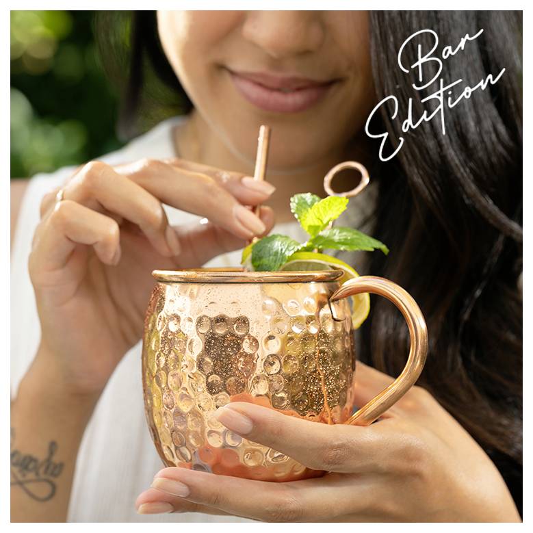 Eine Person, die einen Kupferbecher mit Garnitur hält und durch einen Strohhalm trinkt. Text liest sich 