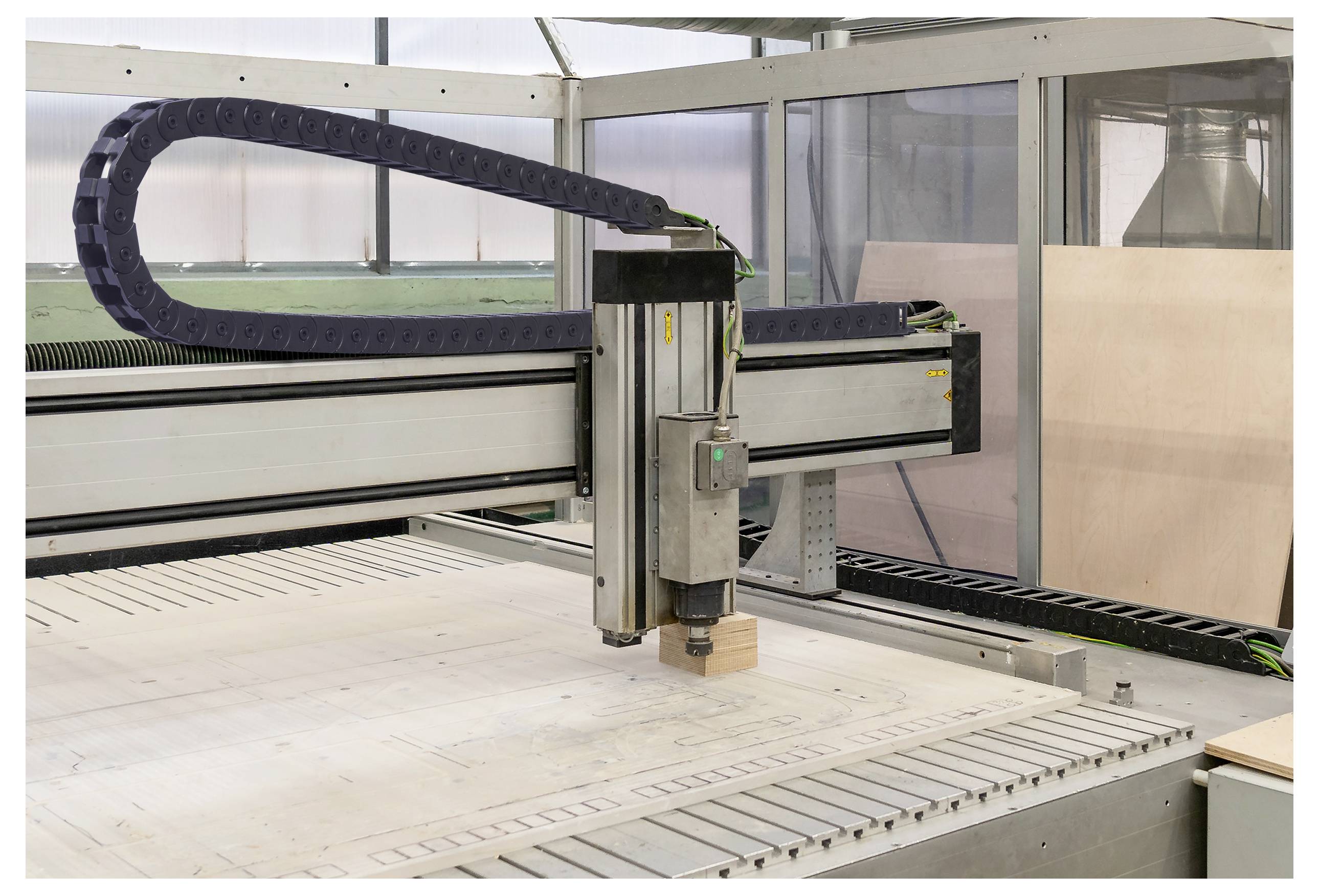 Eine CNC-Maschine schneidet ein Design in ein Holzblatt, mit einem sichtbaren Metallrahmen und einer Schutzabdeckung im Hintergrund.