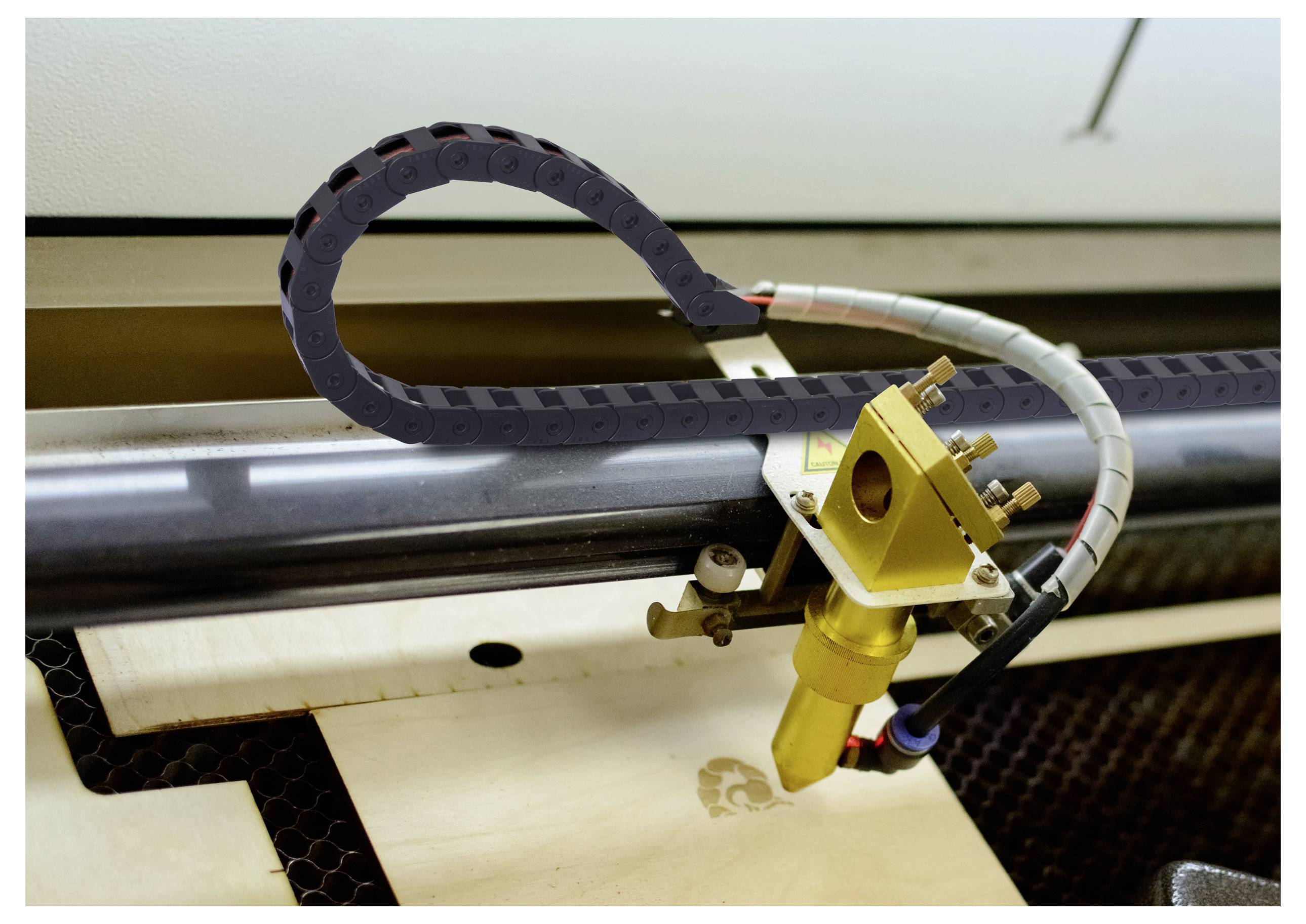 Laserschneidmaschine, die ein Logo auf einem Holzblatt graviert, mit dem Schneidkopf und dem flexiblen Kabel sichtbar über der Arbeitsfläche.
