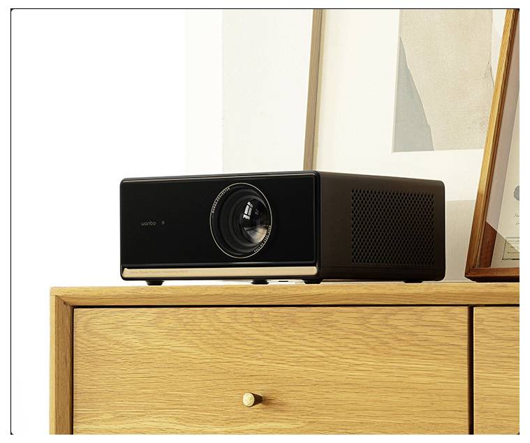 Ein schwarzer Projektor sitzt auf einem hellen Holzschrank an einer weißen Wand, umgeben von modernen Kunstwerken und Dekorationselementen.