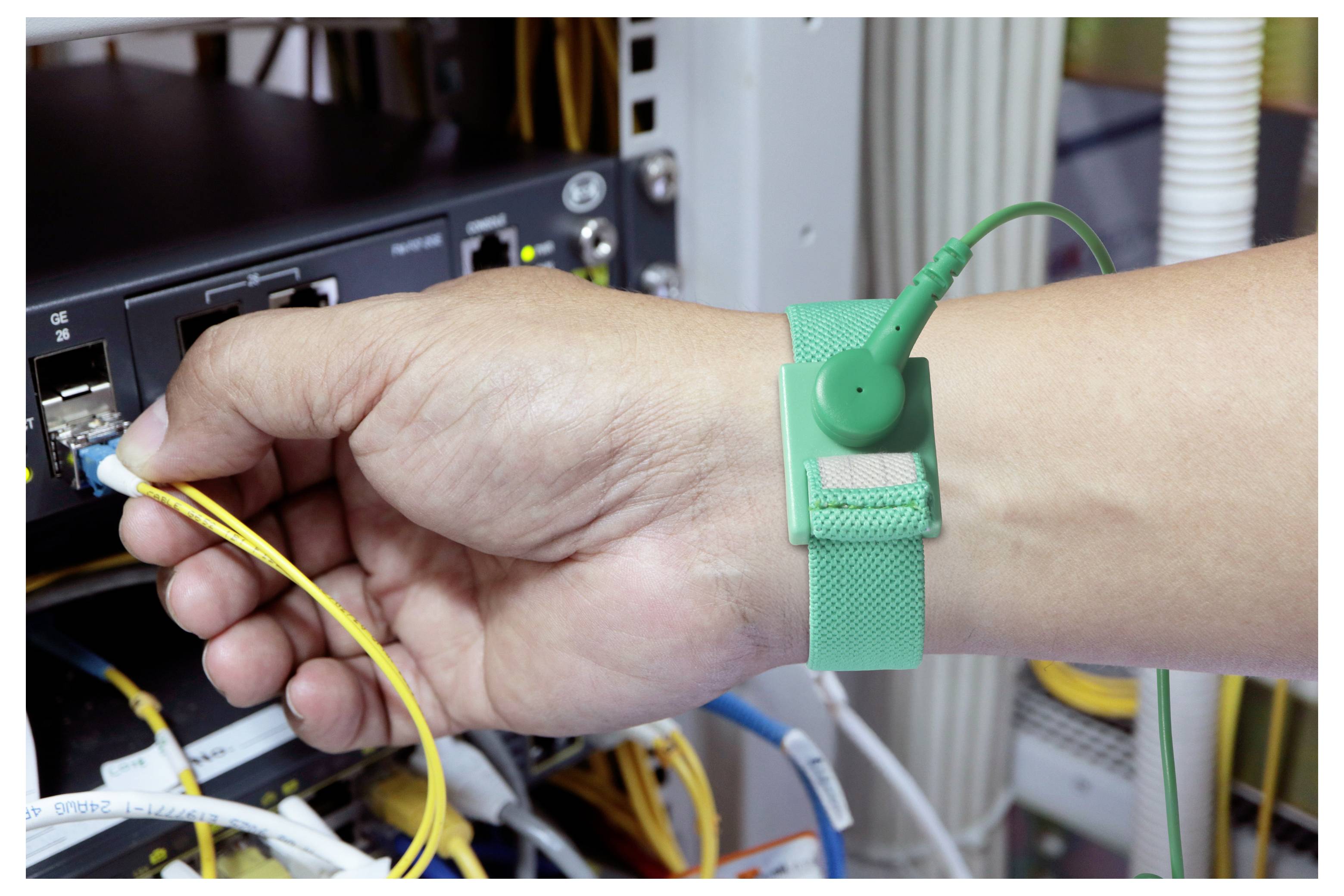 Eine Person, die ein grünes antistatisches Armband trägt, verbindet gelbe Netzwerkkabel mit einem Server-Rack und deutet damit auf Fokus auf IT-Arbeiten oder Wartung hin.