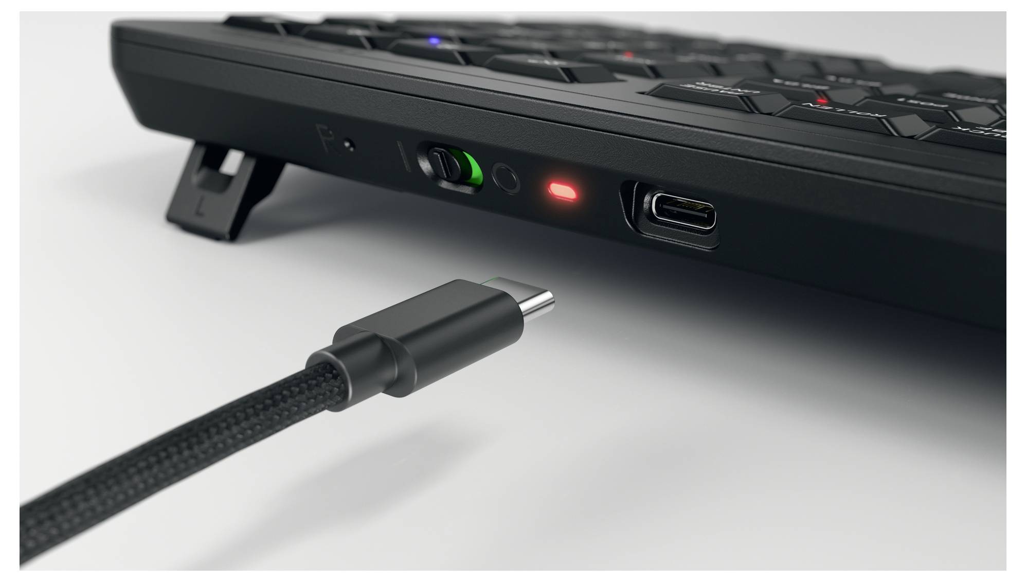Ein USB-C-Kabel nähert sich einer schwarzen Tastatur, bereit zur Verbindung. Die Tastatur hat eine rote Anzeigelampe und einen erhöhten Ständer an der Rückseite.