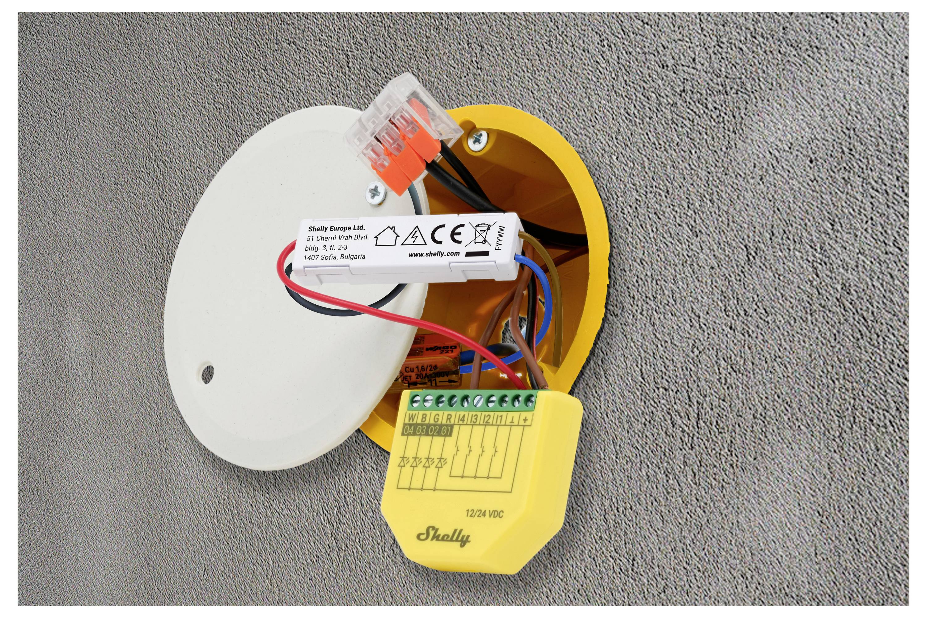 Eine offene elektrische Verteilerdose in einer Wand mit freiliegender Verkabelung und Komponenten. Die Ausführung umfasst eine weiße Abdeckung, Klemmenblöcke und Beschriftungen.