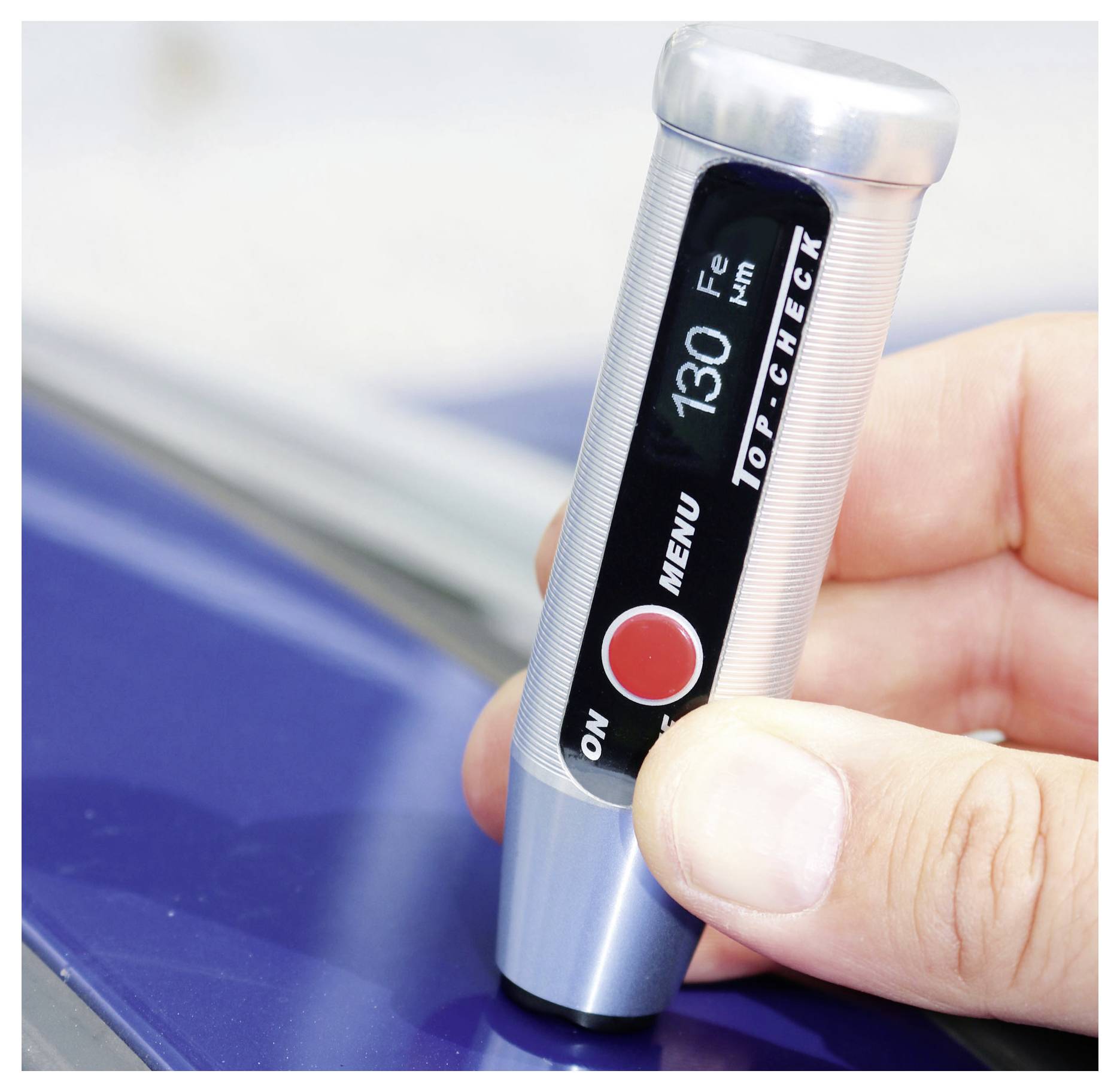 Hand hält ein tragbares digitales Thermometer gegen eine blaue Oberfläche, auf dem Display werden 130 und 'Top-Check' angezeigt.