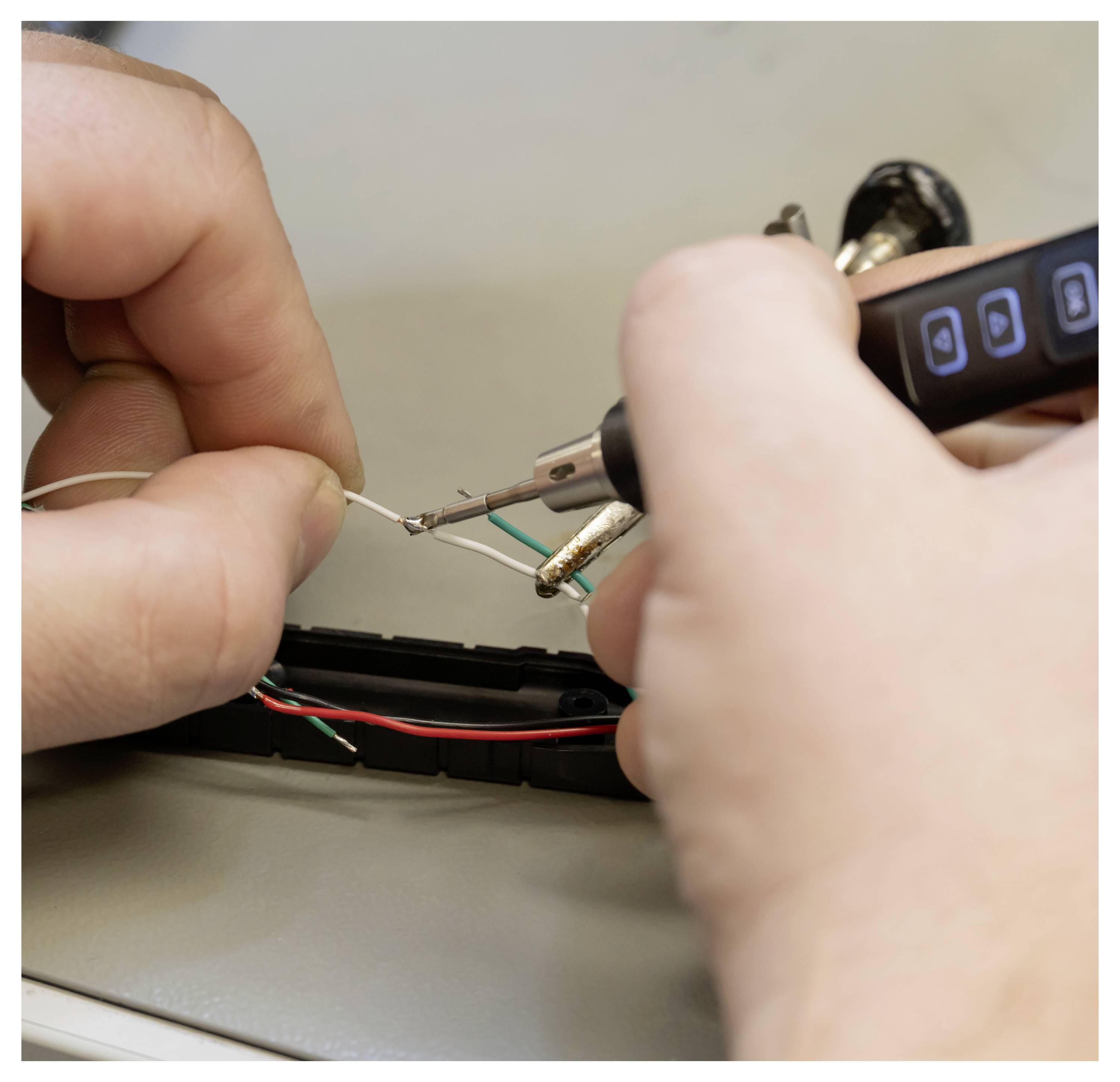 Hände, die einen Lötkolben verwenden, um dünne Drähte in einem kleinen elektronischen Gerät während der Reparatur zu verbinden.