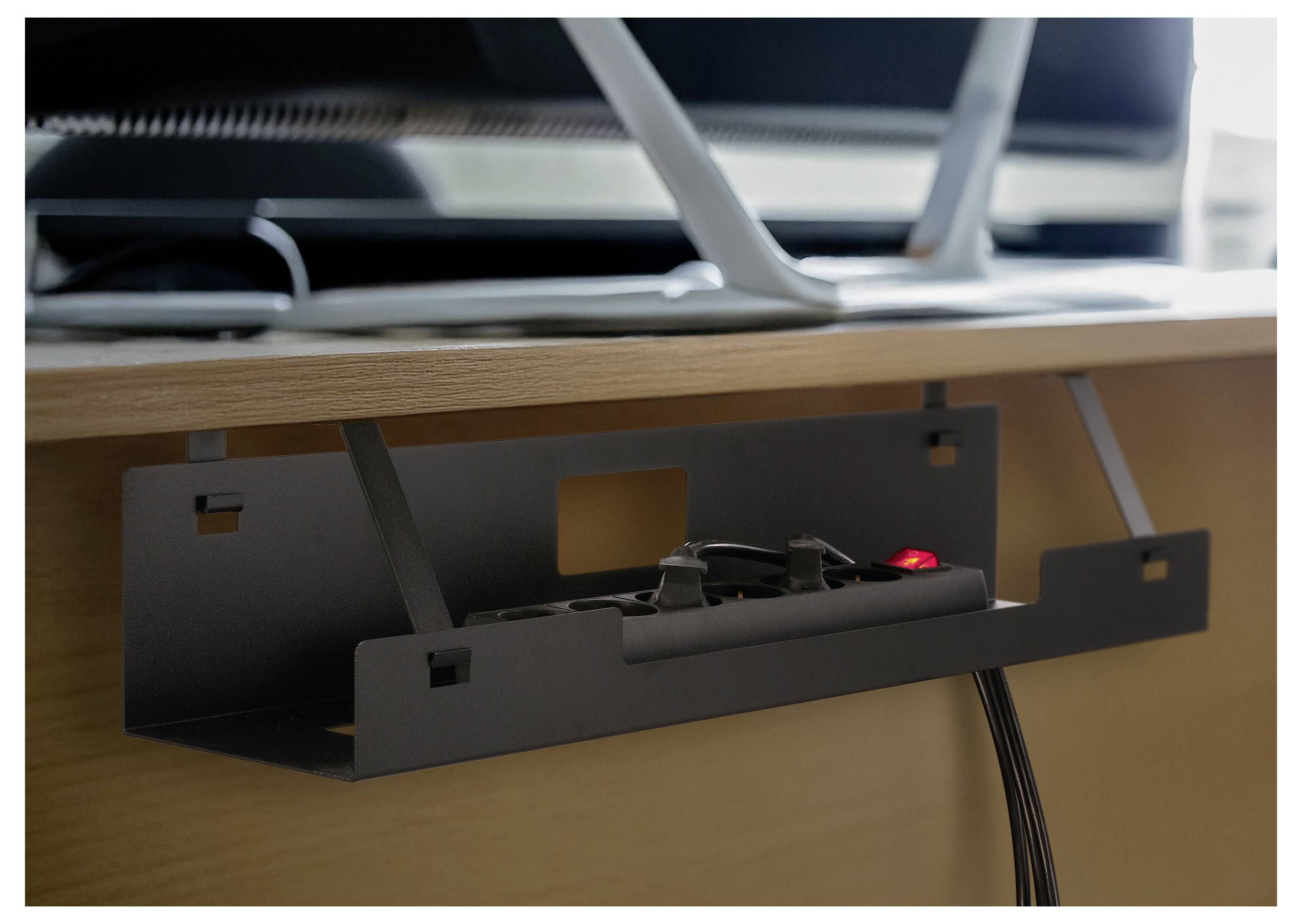 Kabelorganizer unter dem Schreibtisch mit Stromleiste und angeschlossenen Kabeln, die unter einem Holzschreibtisch montiert sind und ein rotes Anzeigelicht zeigen.