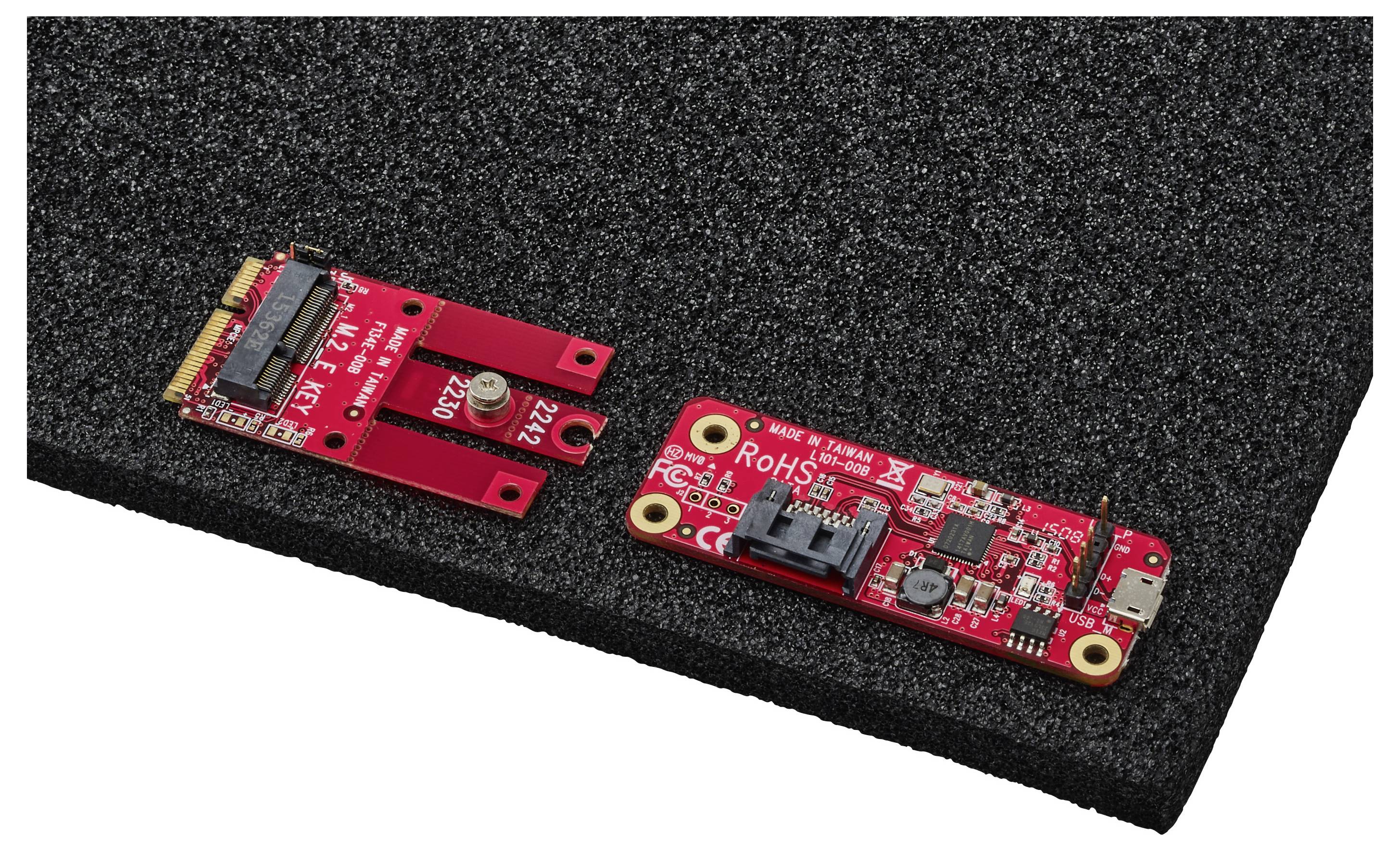 Zwei rote Leiterplatten mit Beschriftungen, auf schwarzem Schaumstoff platziert. Eine Platine hat einen Stecker und die andere hat verschiedene Komponenten und einen USB-Anschluss.