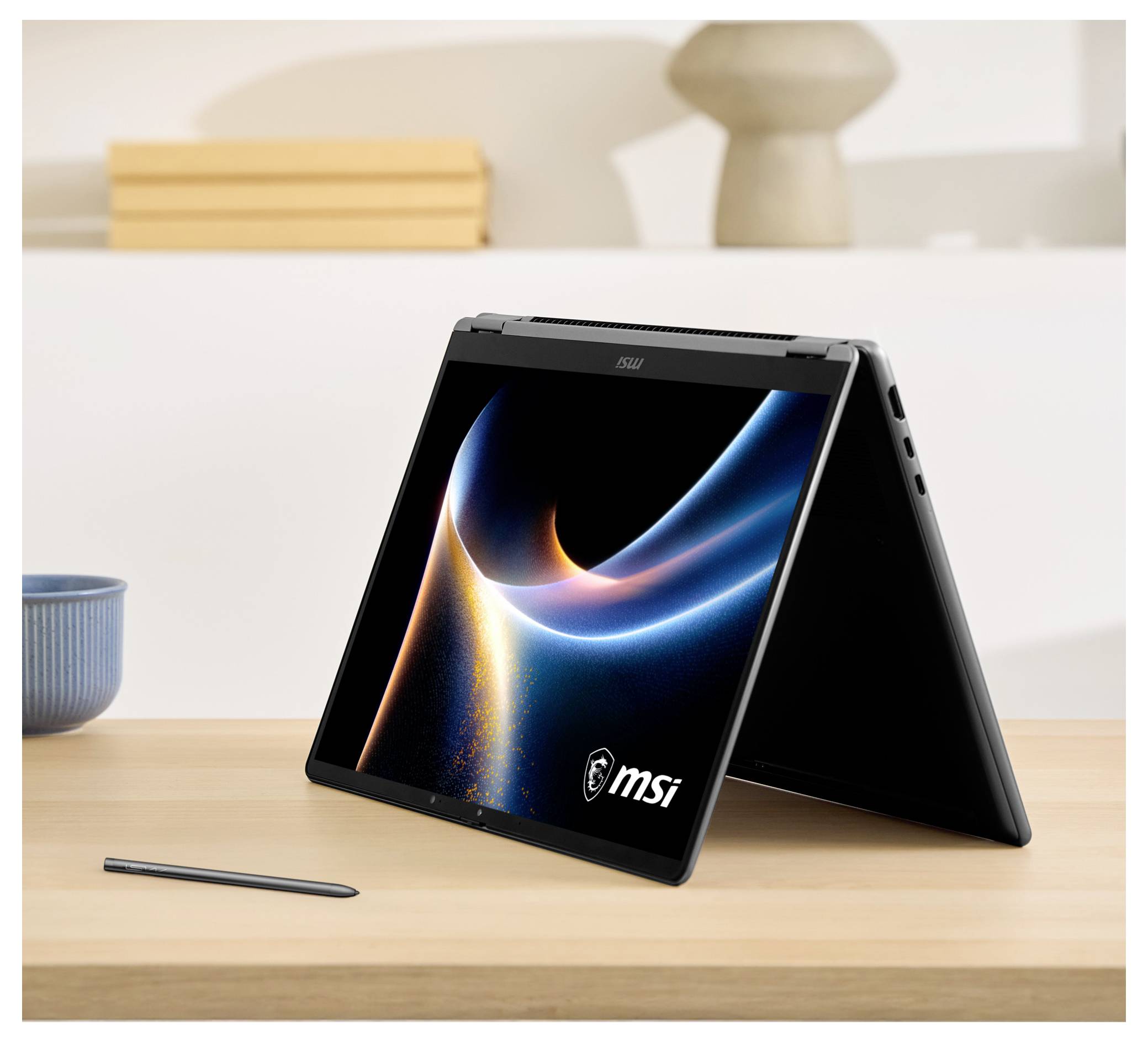 Ein Laptop im Zeltmodus auf einem Schreibtisch mit einem Stift in der Nähe, der ein dynamisches Wirbelmuster auf dem Bildschirm anzeigt, mit der Marke „MSI