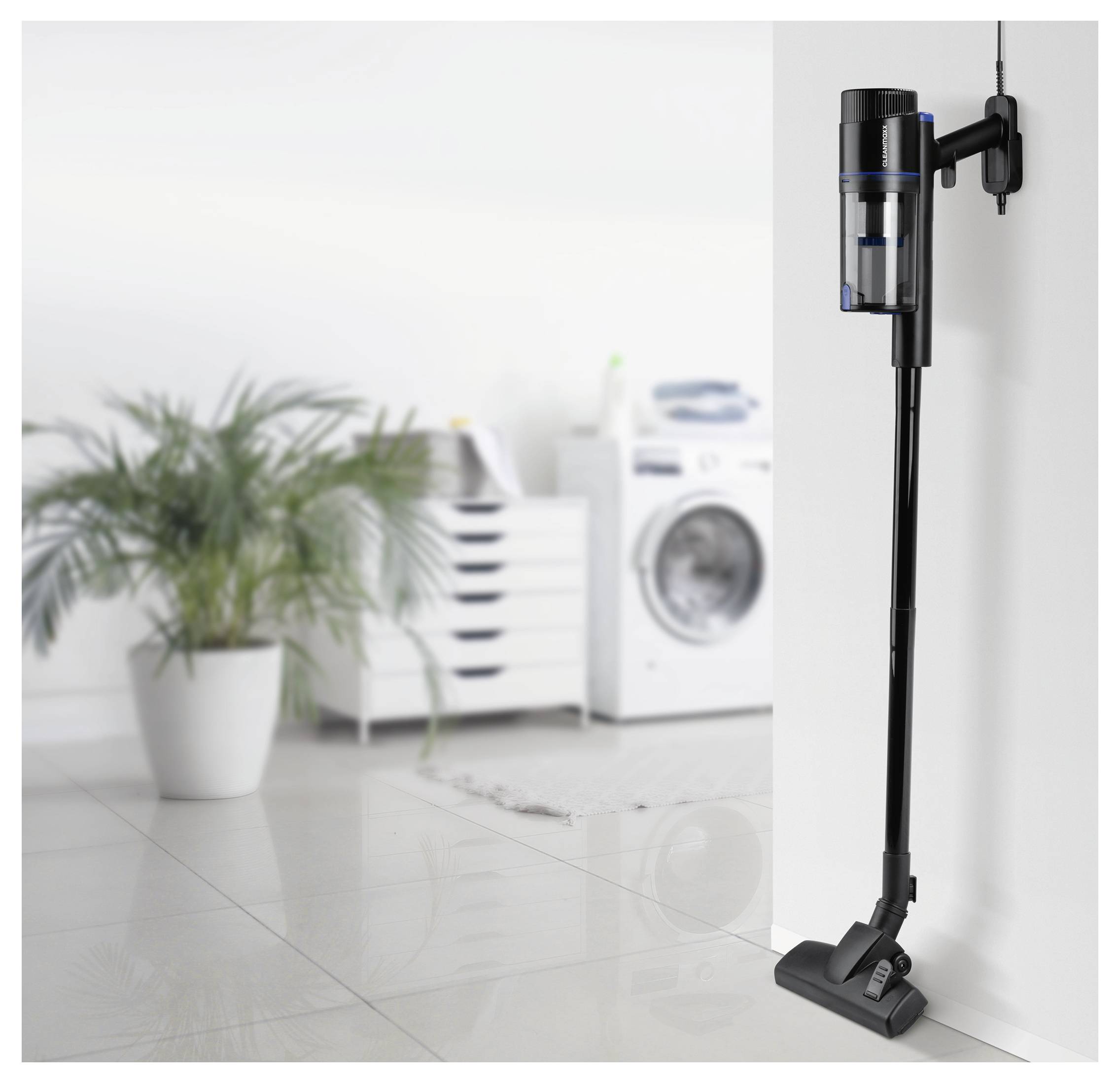 Ein schnurloses Staubsaugergerät ist an einer Wand in einem modernen Waschzimmer montiert. Eine Waschmaschine und eine Topfpflanze sind im Hintergrund sichtbar.