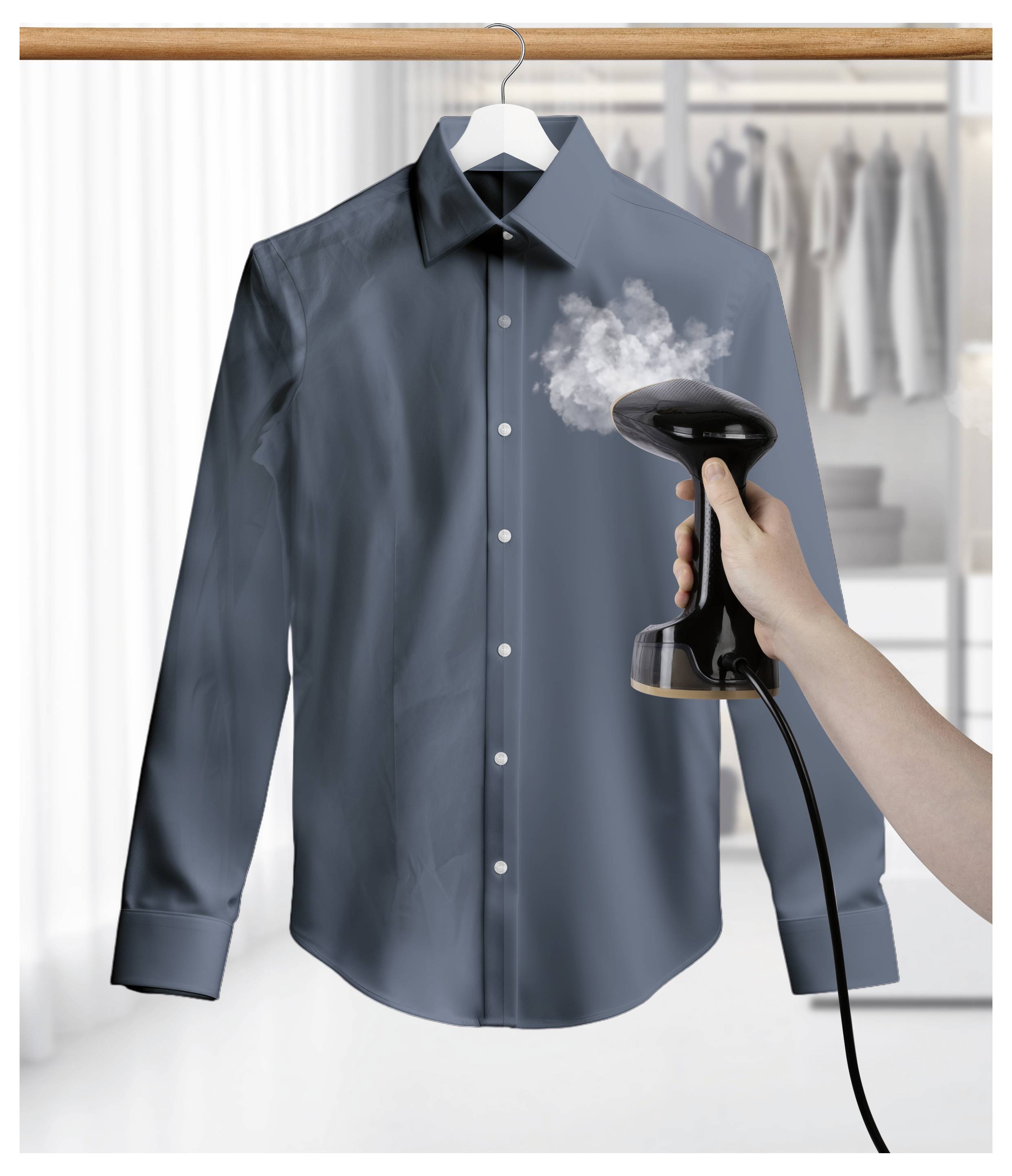 Eine Hand benutzt einen Dampfreiniger, um Falten aus einem dunklen Hemd zu entfernen, das an einem Kleiderbügel hängt, mit einem unscharfen Kleiderschrank im Hintergrund.