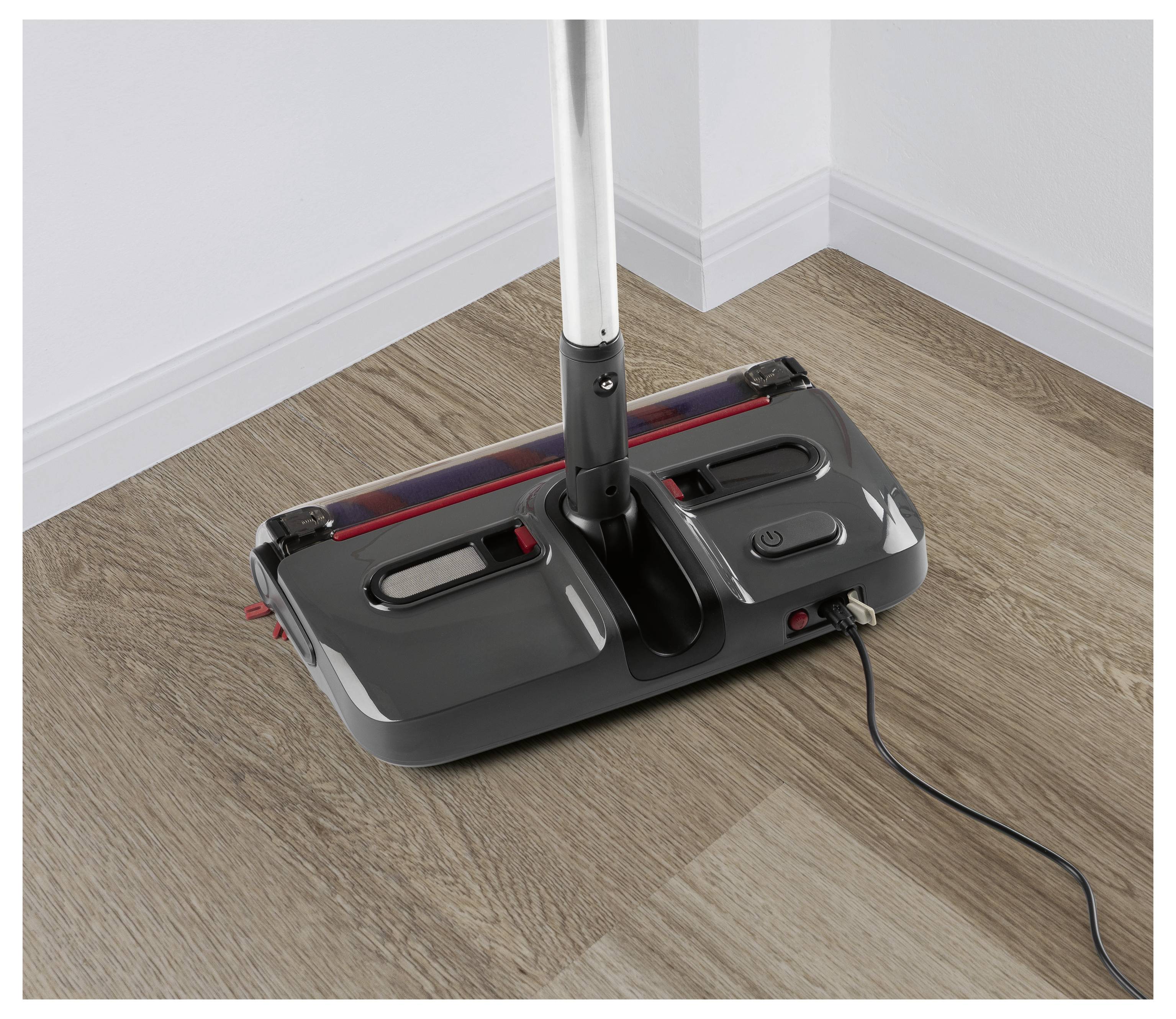 Elektrischer Bodenkehrer auf einem Holzboden, eingesteckt und einsatzbereit.