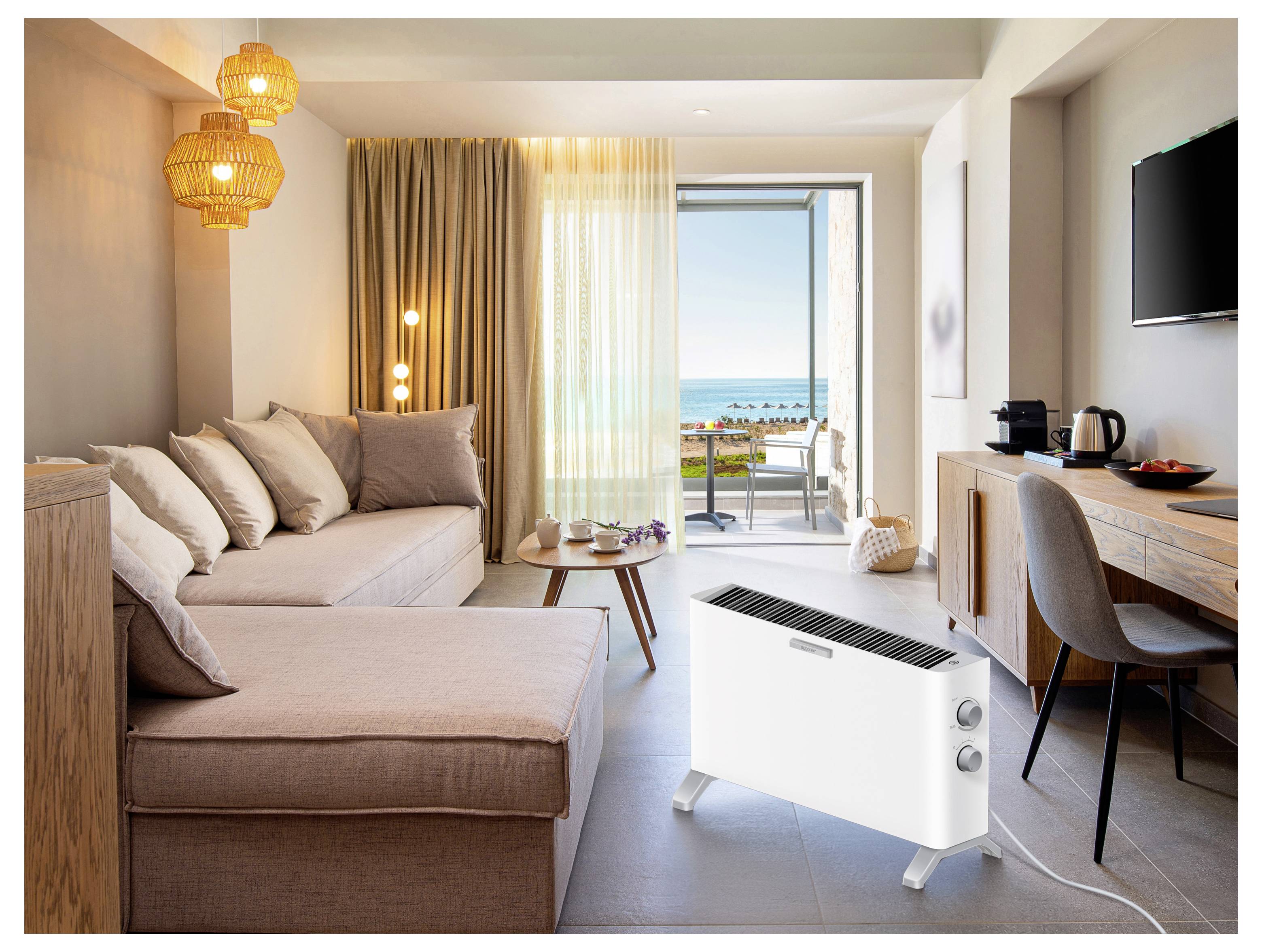 Modernes Hotelzimmer mit Sofa, Schreibtisch und Balkon mit Meerblick, mit einem tragbaren weißen Heizer im Vordergrund.