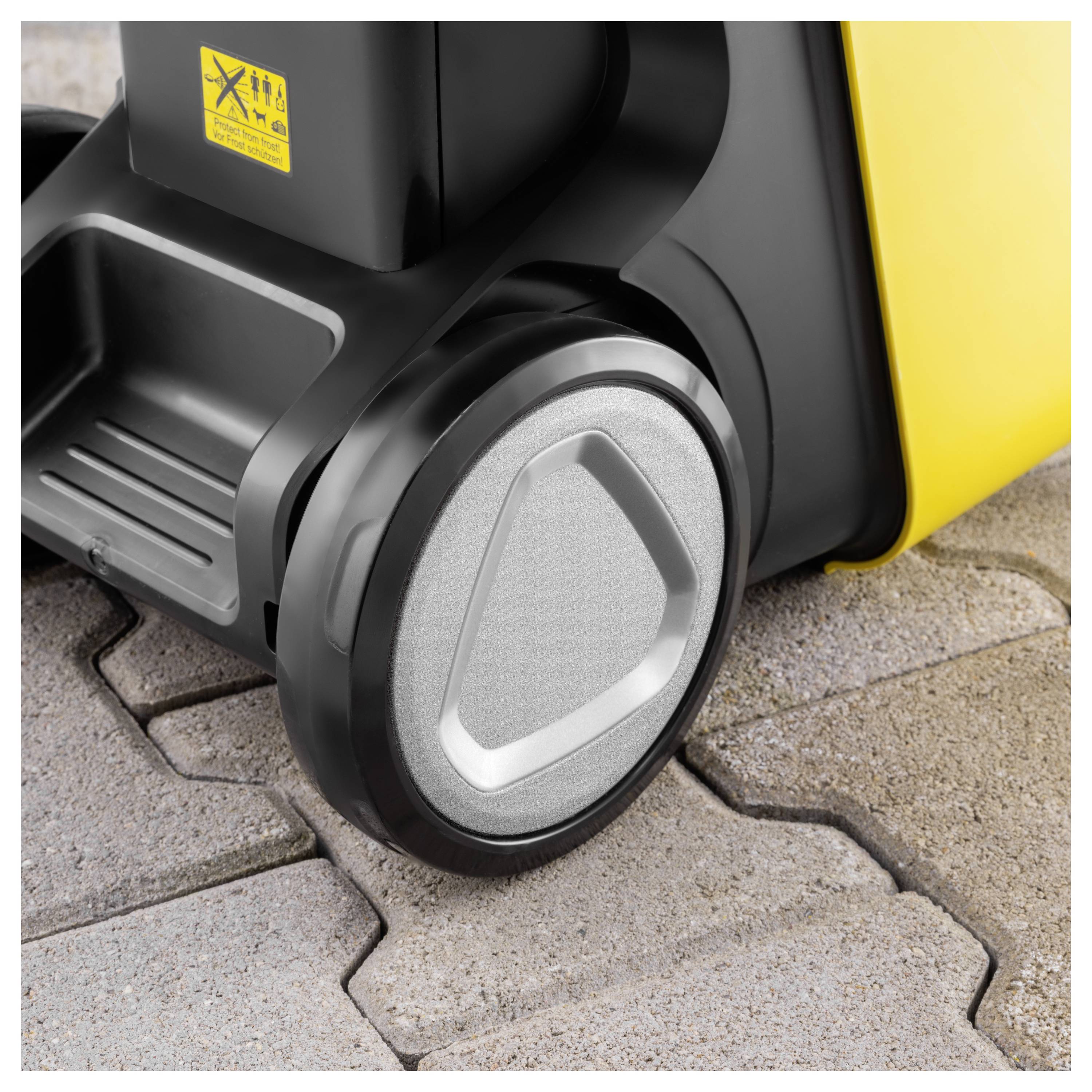 Das Rad einer schwarz-gelben Maschine auf einer strukturierten Betonoberfläche. Das Bild hebt das Design und die Langlebigkeit des Rades hervor.