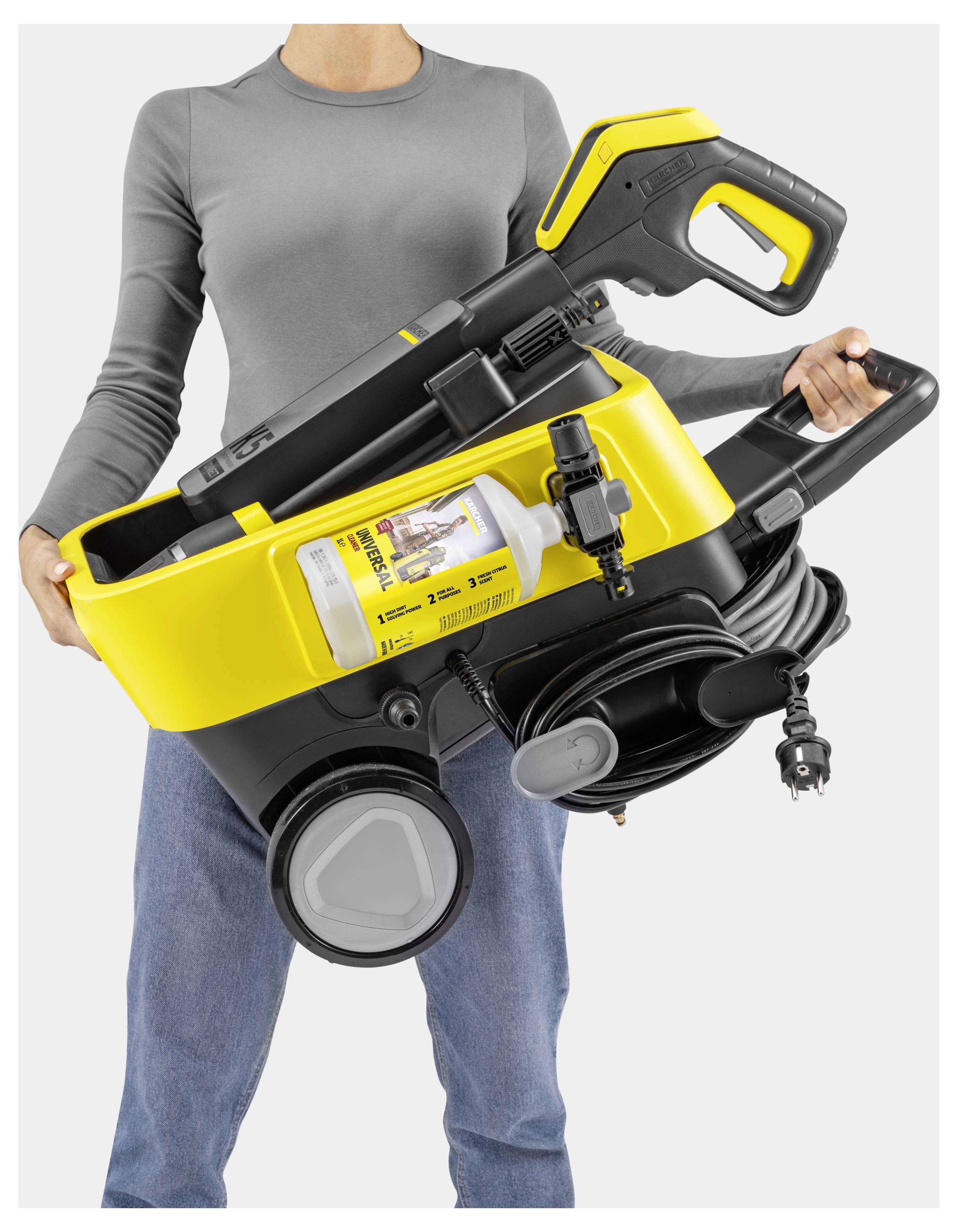 Eine Person, die einen gelb-schwarzen tragbaren Hochdruckreiniger mit einem integrierten Fach für Reinigungsmittelflaschen und einem ordentlich aufgerolltem Kabel hält.