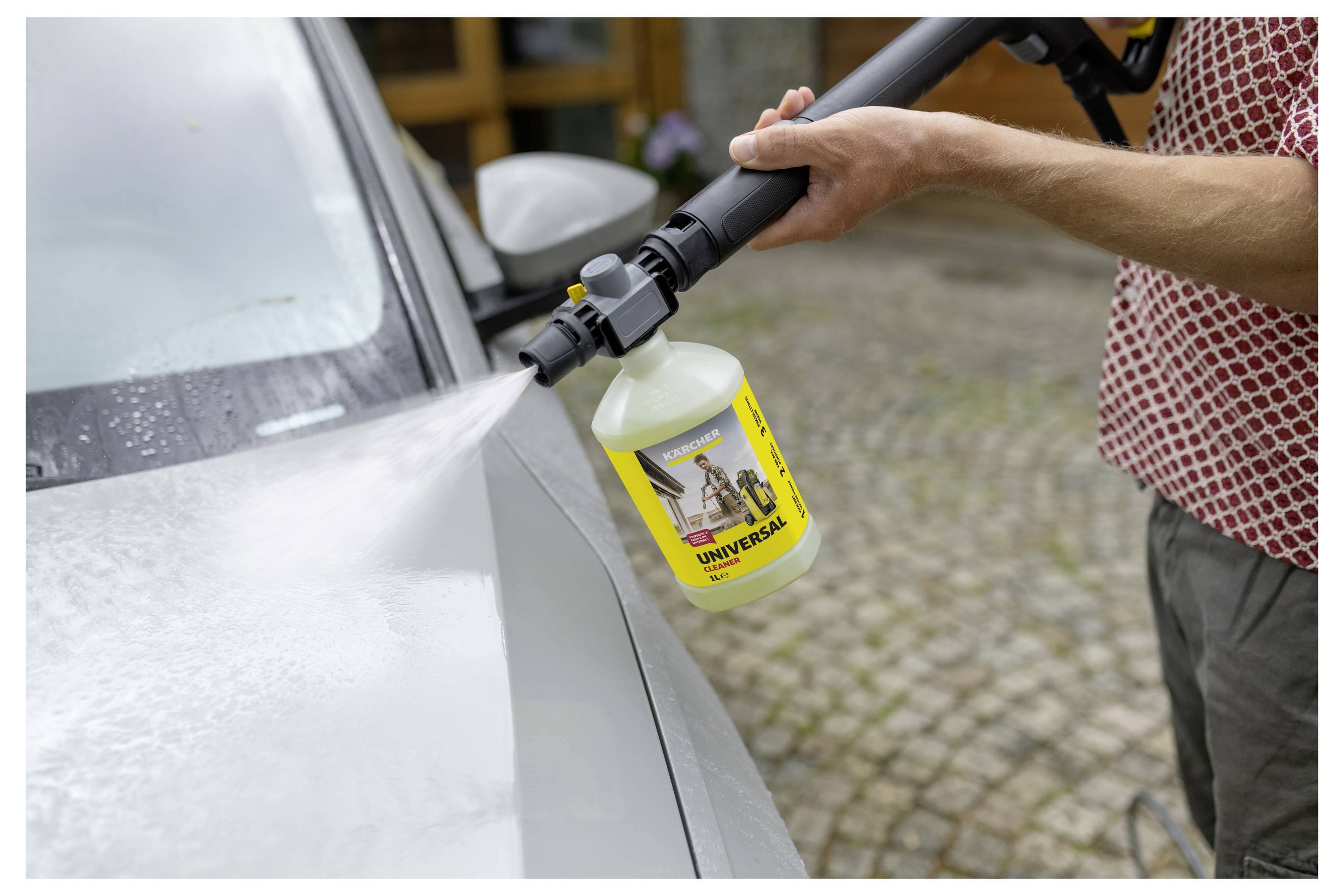 Eine Person nutzt einen Hochdruckreiniger mit einer Reinigungsmittelanlage an einem Auto und konzentriert sich dabei auf einen Seifenschaum, der die Fahrzeugoberfläche zielt.