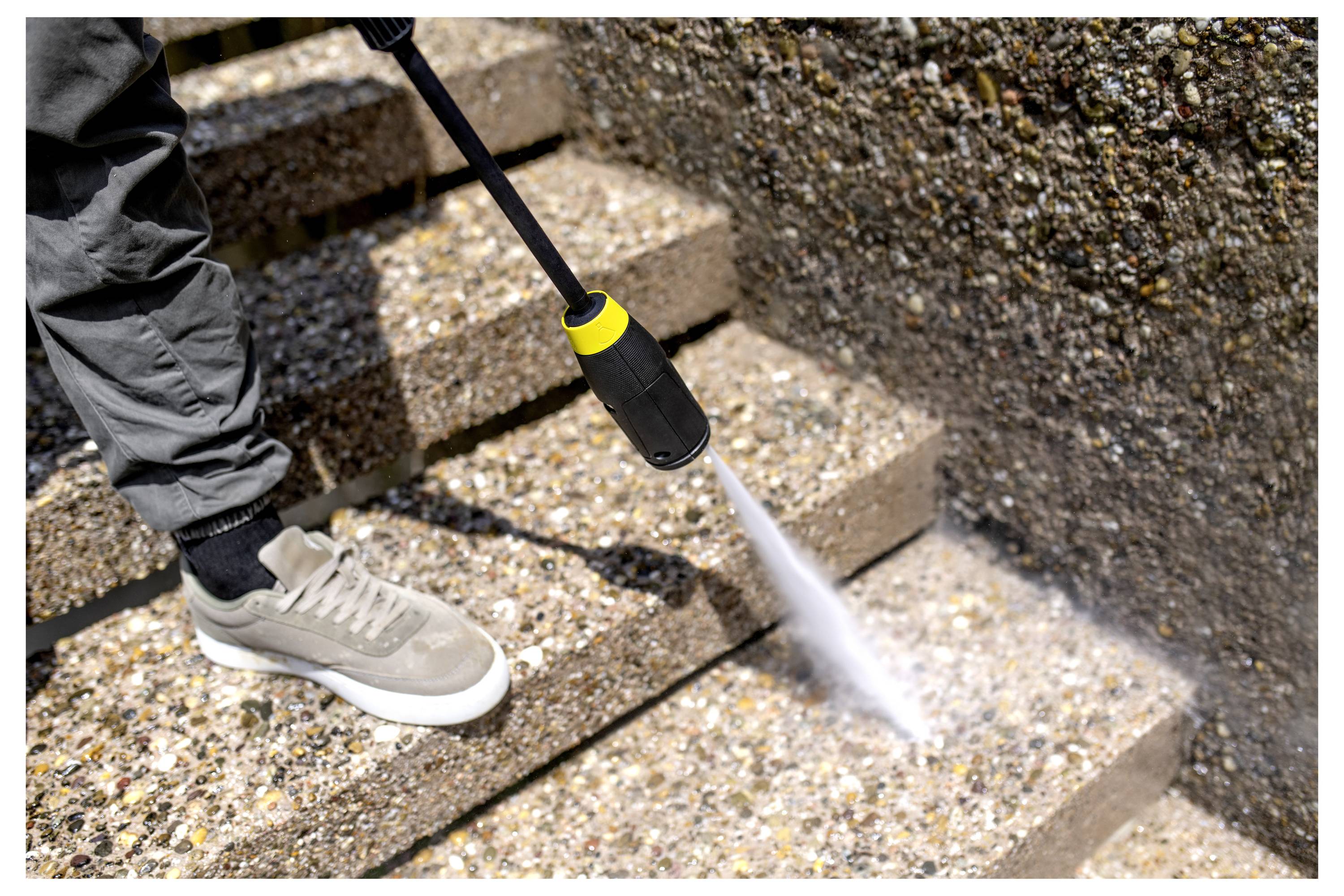 Eine Person nutzt einen Hochdruckreiniger, um eine Reihe von außenliegenden Betonstufen zu reinigen und dabei Schmutz und Ablagerungen zu entfernen.