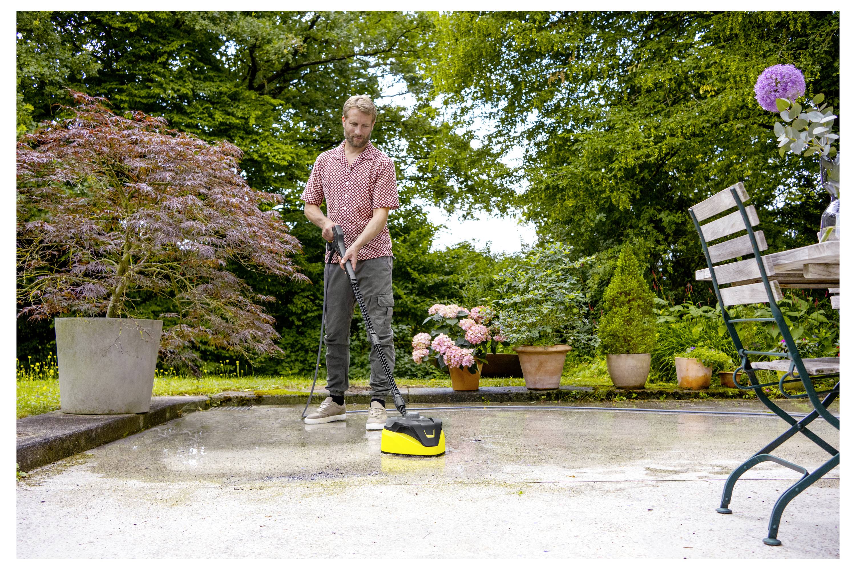 Eine Person reinigt eine Terrasse mit einem Hochdruckreiniger in einer Gartenumgebung, umgeben von Topfpflanzen und Gartenmöbeln.