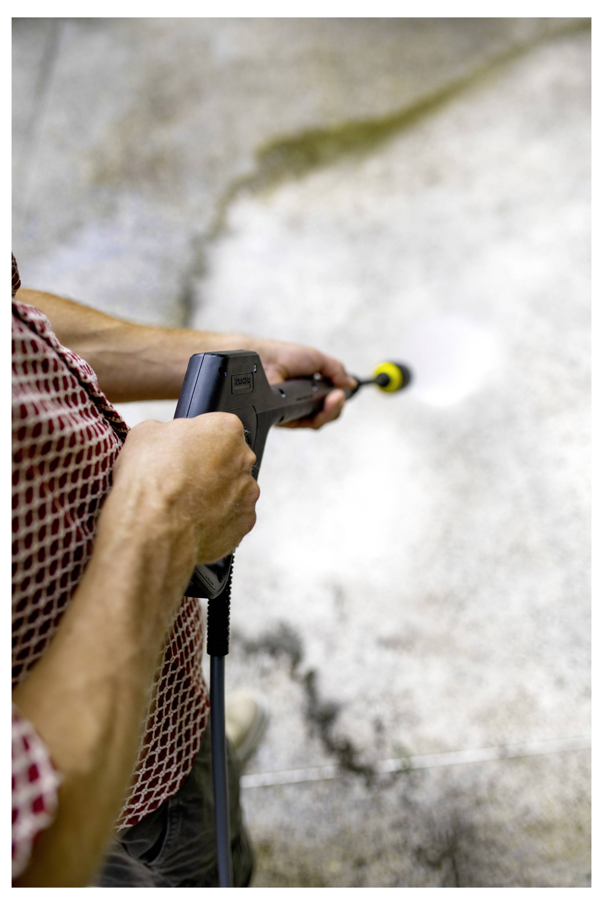 Eine Person, die eine befleckte Betonoberfläche mit einem Hochdruckreiniger reinigt, mit sichtbarem Kontrast zwischen den gereinigten und schmutzigen Bereichen.