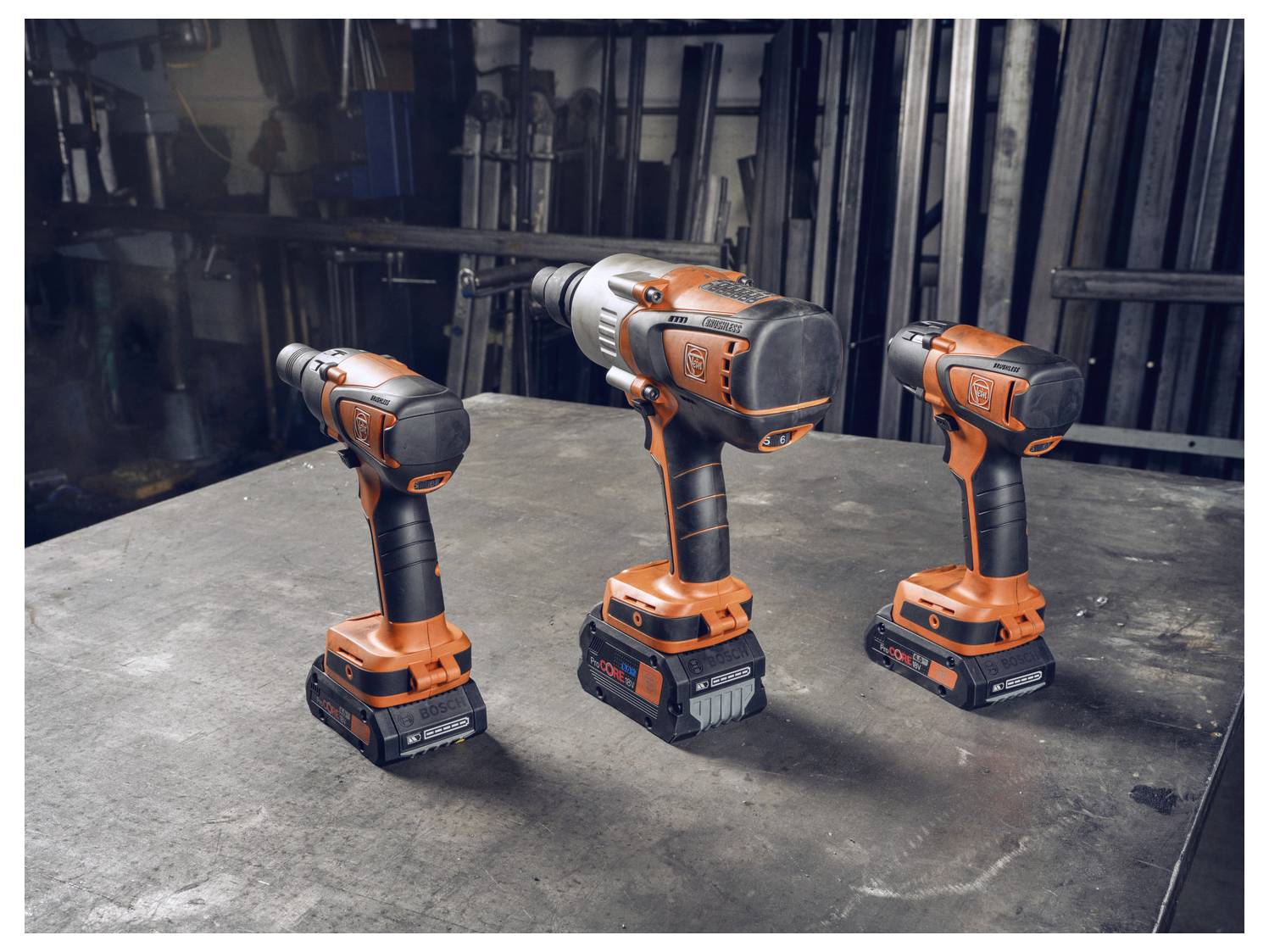 Drei kabellose Elektroschrauber sind auf einer Werkbank in einer Werkstatt ausgestellt und zeigen ihr ergonomisches Design und orange Akzente.