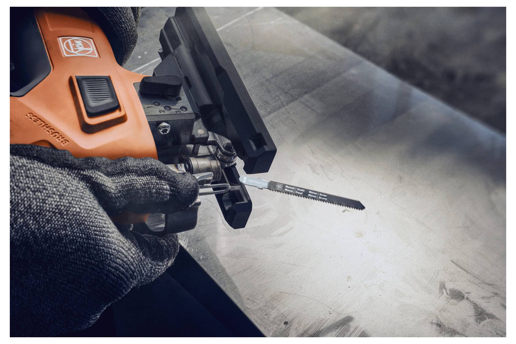 Eine Person trägt Handschuhe und benutzt ein orange-schwarzes Elektrowerkzeug, um ein Stück Metall auf einer Werkbank zu schneiden. Der Bereich ist gut beleuchtet.