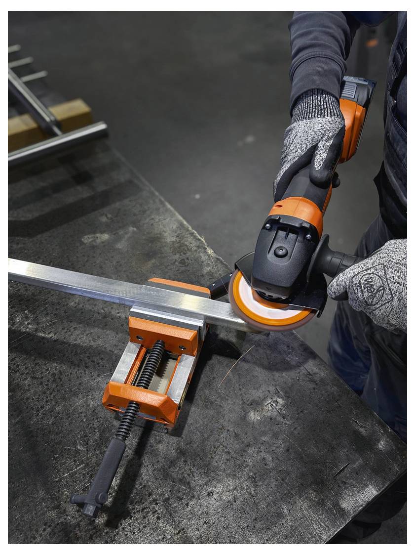 Eine Person, die Schutzhandschuhe trägt, benutzt einen orange-schwarzen Winkelschleifer, um Metall zu schneiden, das in einem Schraubstock auf einer Werkbank gesichert ist.