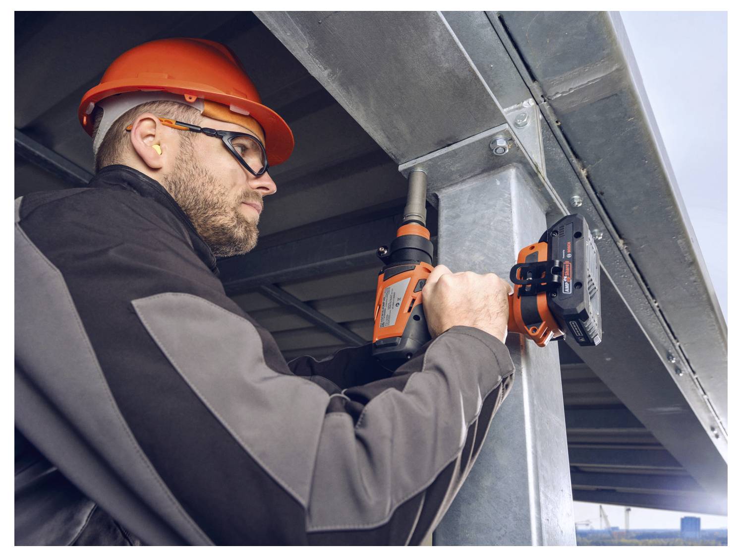 Ein Bauarbeiter in Schutzausrüstung sichert einen Metallträger auf einer Baustelle mit einem Elektroschrauber und konzentriert sich dabei auf Sicherheit und Präzision.