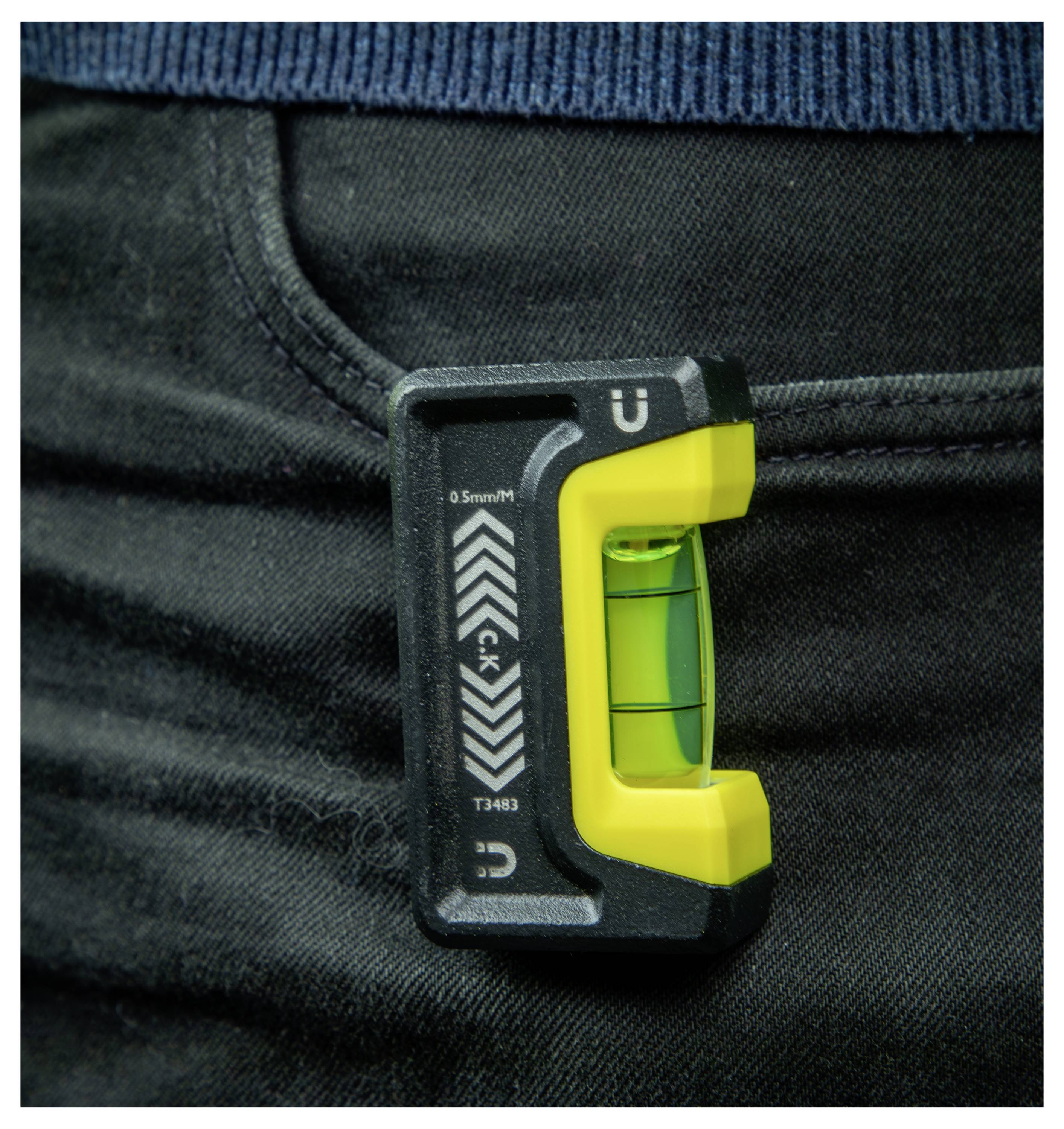 Ein kleines, grünes, U-förmiges Wasserwaagen-Werkzeug, das an einer schwarzen Jeanstasche befestigt ist.