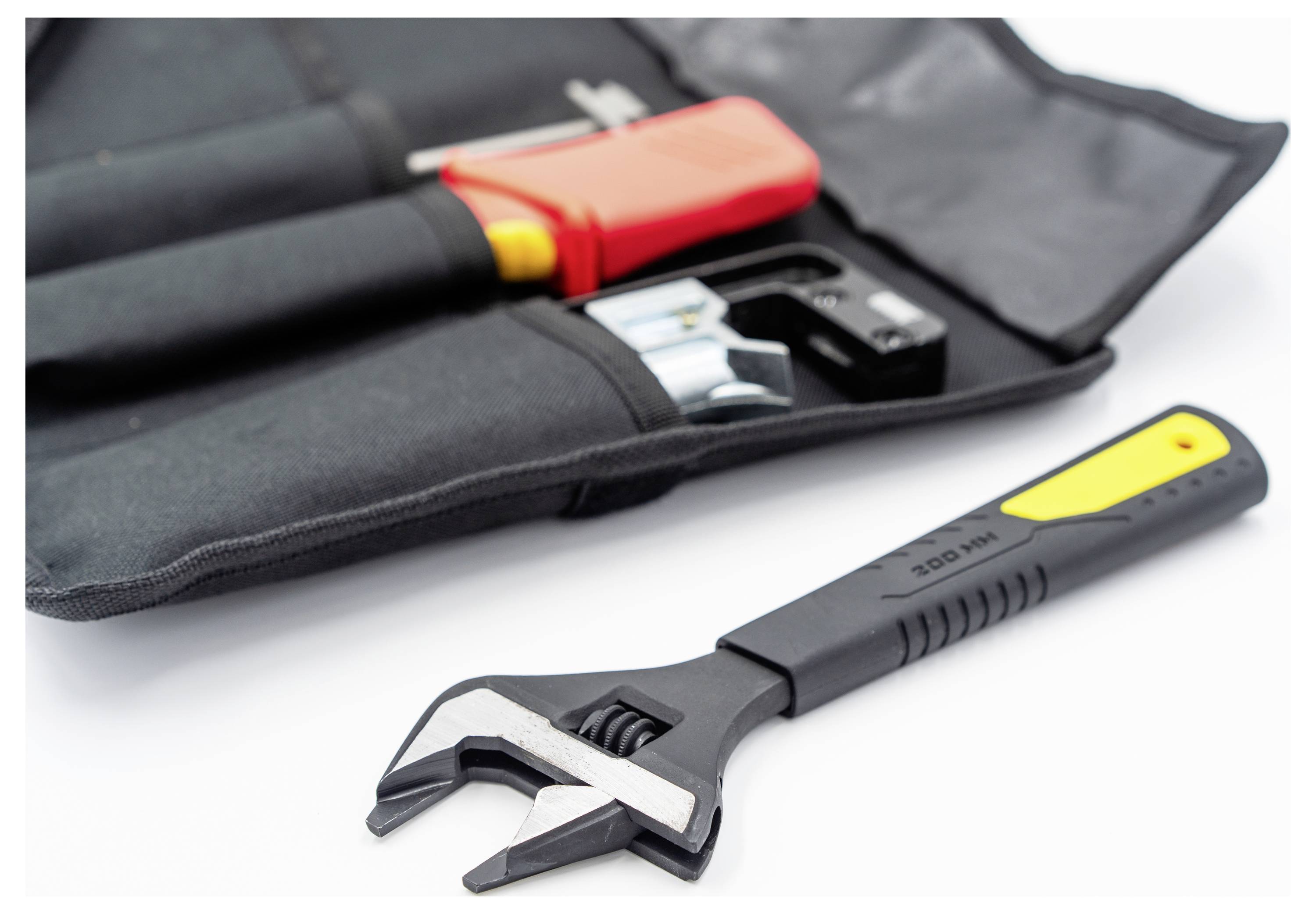 Ein schwarz-gelber verstellbarer Schraubenschlüssel liegt neben einer offenen Werkzeugtasche mit einem Werkzeug mit rotem Griff und weiteren Eisenwaren auf einer weißen Oberfläche.