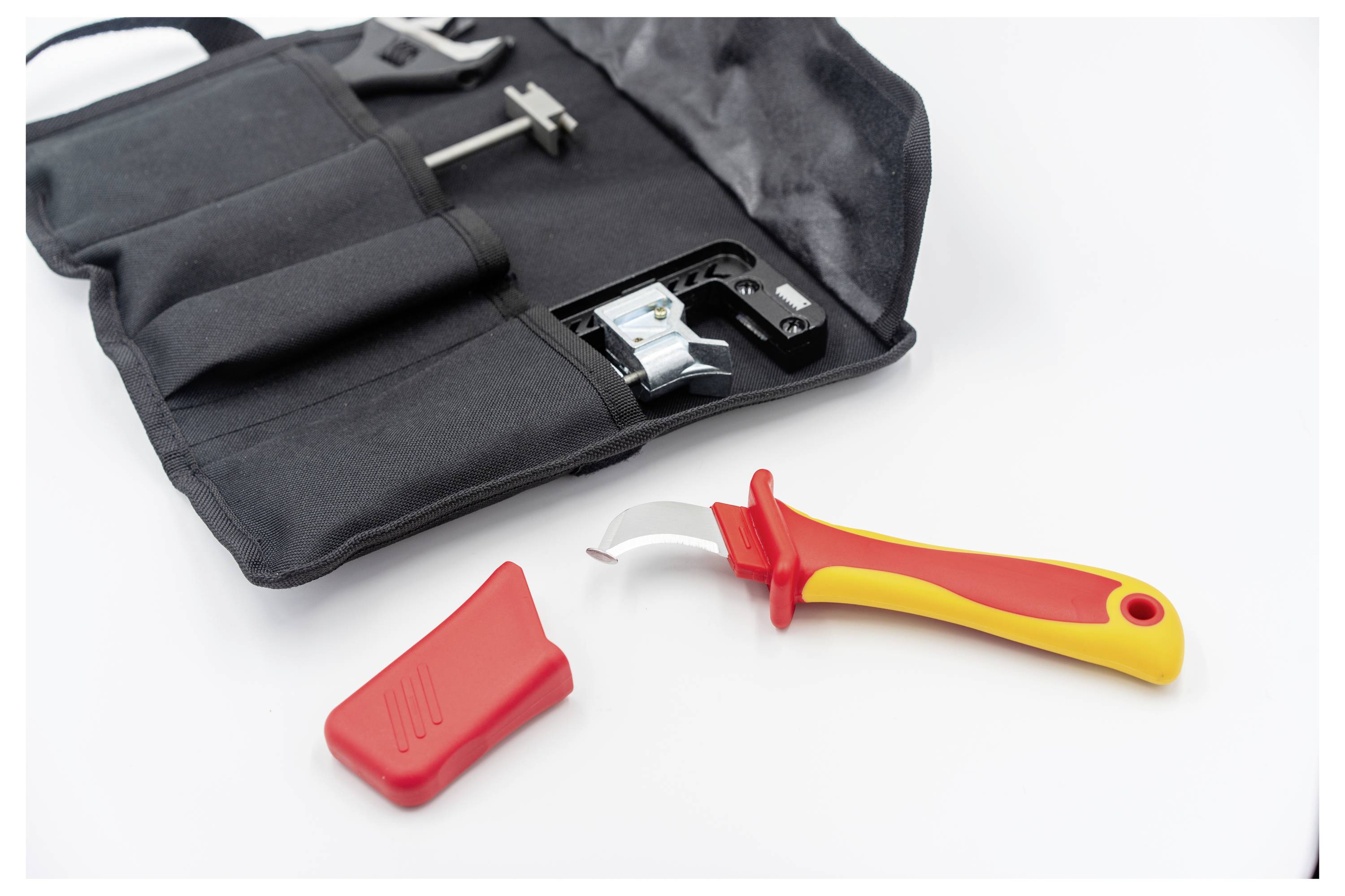 Ein Sicherheitsdosenöffner mit roten und gelben Griffen wird aus seinem schwarzen Transportbeutel entnommen, wobei eine rote Abdeckung daneben platziert ist.