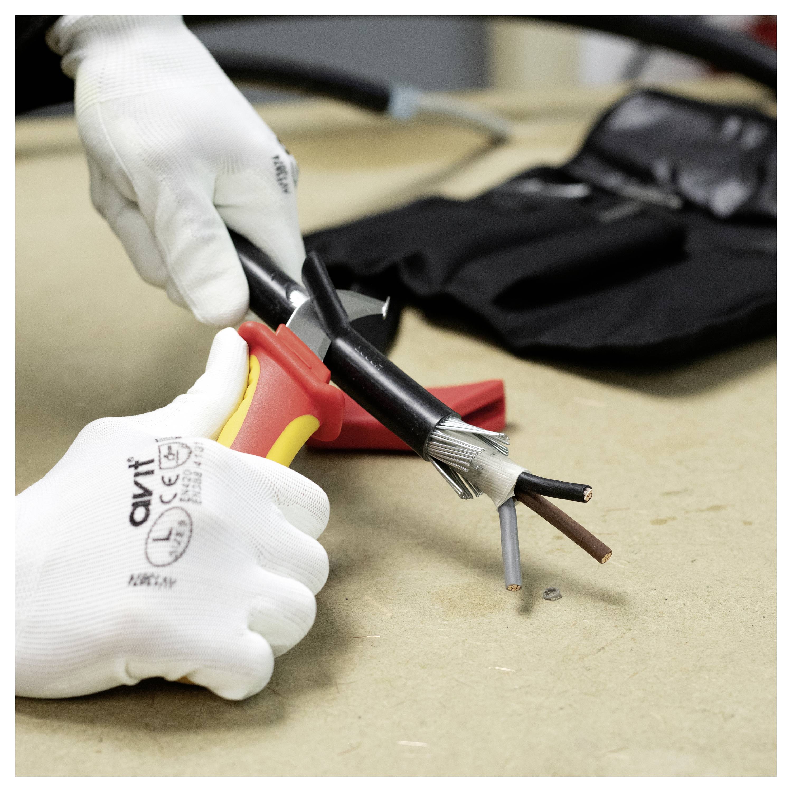 Eine Person, die Schutzhandschuhe trägt, benutzt ein Werkzeug, um die äußere Isolierung eines Elektrokabels abzustreifen und mehrere Drähte freizulegen.