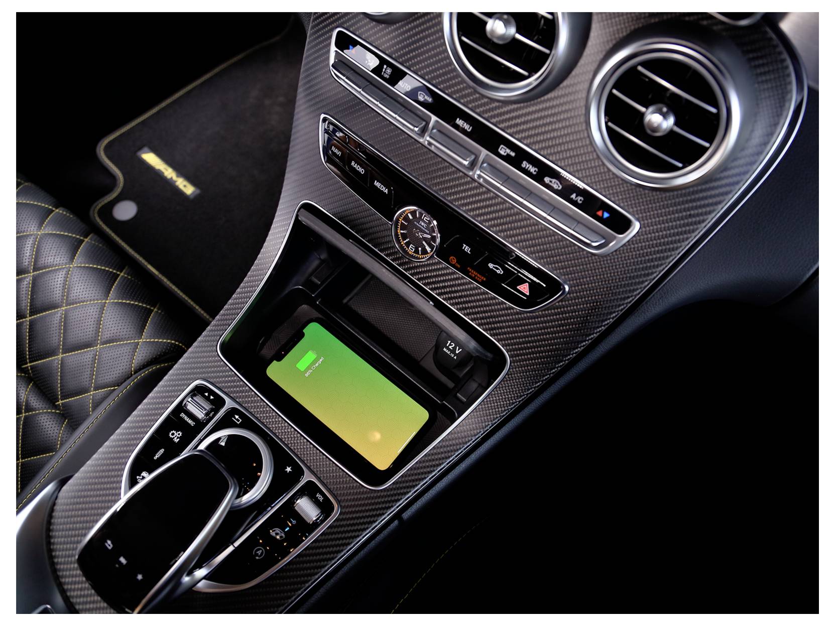 Mittelkonsole des Autos mit kabellosen Ladeflächen, Klimasteuerungen, Uhr, Luftauslassen und Schaltwahlhebel; grüne Telefonladenanzeigelampe sichtbar.