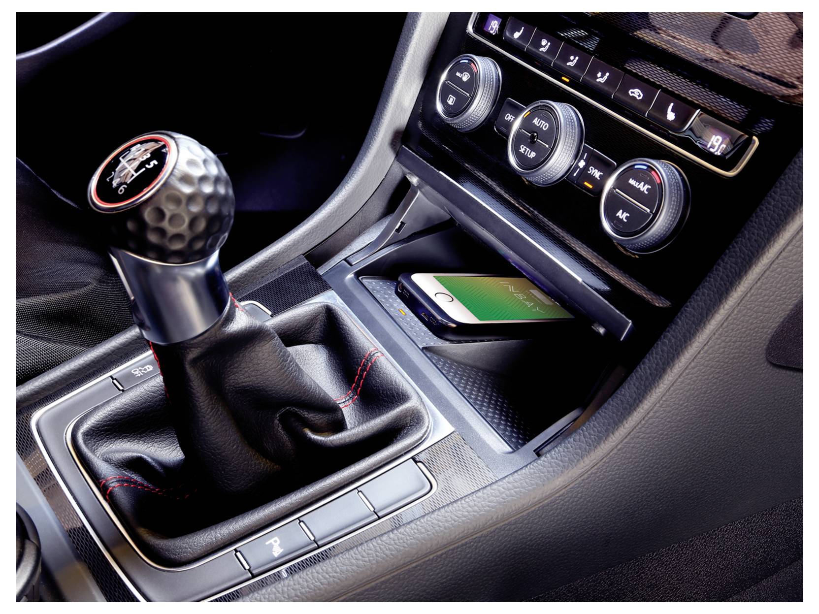 Innenraum eines Autos mit Mittelkonsole mit manuellem Schaltknüppel, Klimaanlage-Steuerungen und einem Smartphone im Ablagefach.