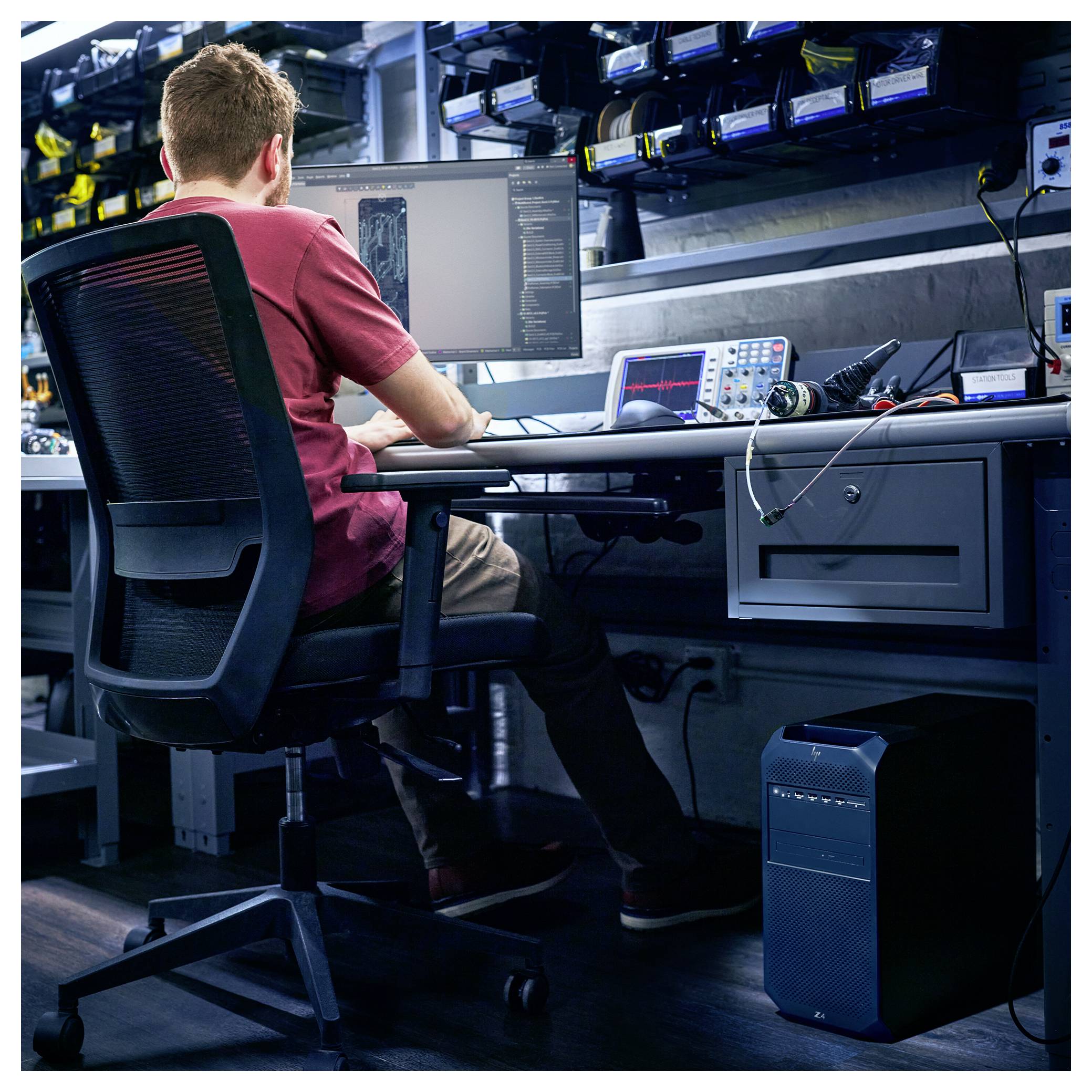 Eine Person, die an einem Schreibtisch mit mehreren Monitoren und elektronischer Ausrüstung arbeitet und sich auf Programmierung oder digitale Aufgaben in einer Tech-Labor-Umgebung konzentriert.