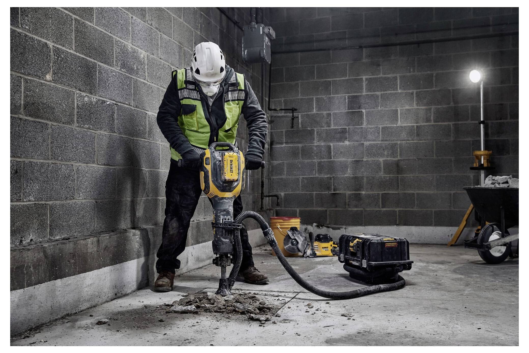 Arbeiter in Schutzausrüstung bedient einen Presslufthammer auf einem Betonboden in einer dunkel beleuchteten Industrieumgebung.